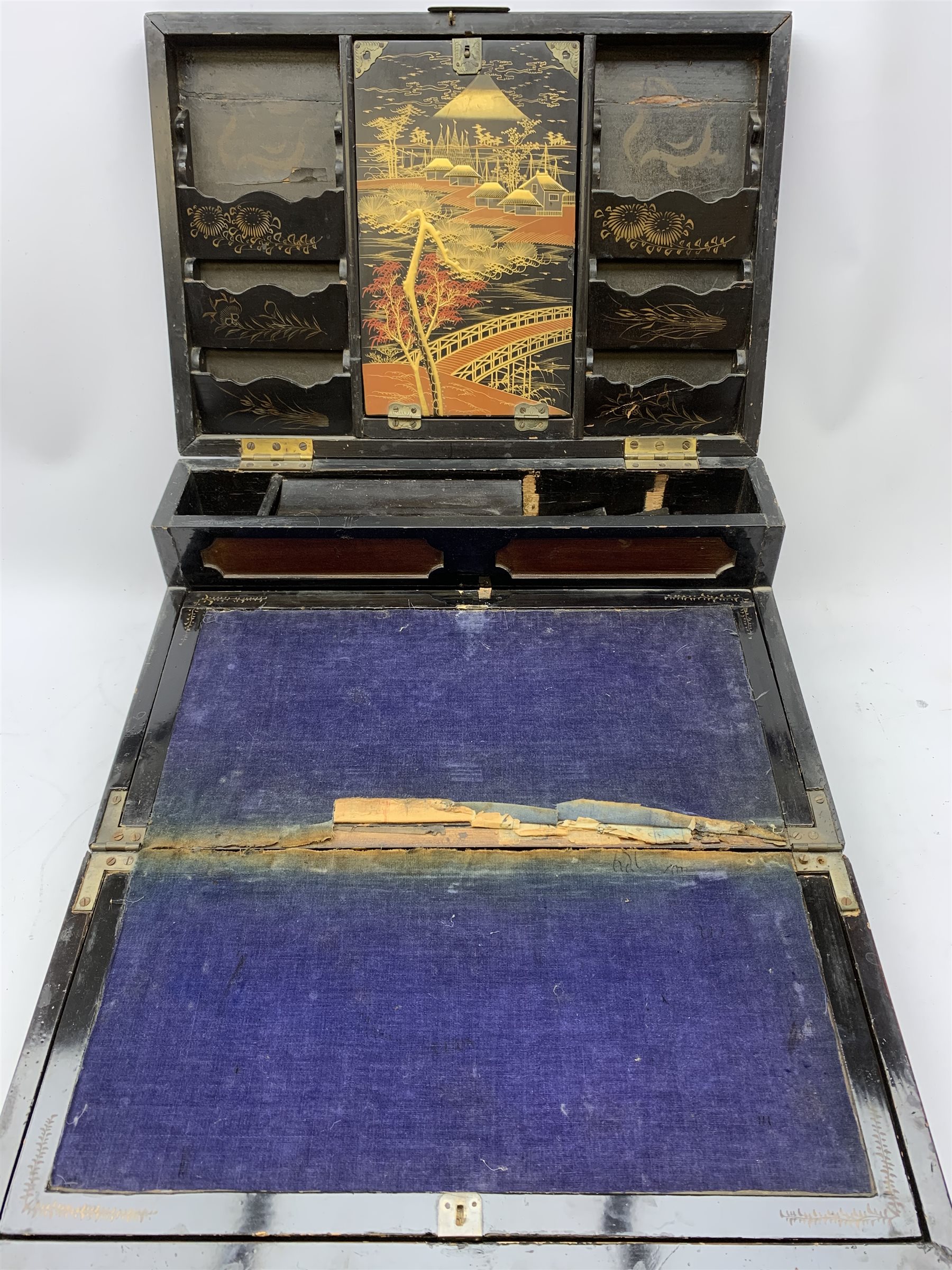  A 20th century Chinese black lacquer and gilt detailed writing box, decorated with figures, pagodas and cranes amidst a mountainous landscape, the hinged cover opening to reveal a compartmented interior and fold out baize lined slope, H20cm L46.5cm D31.5cm.   
