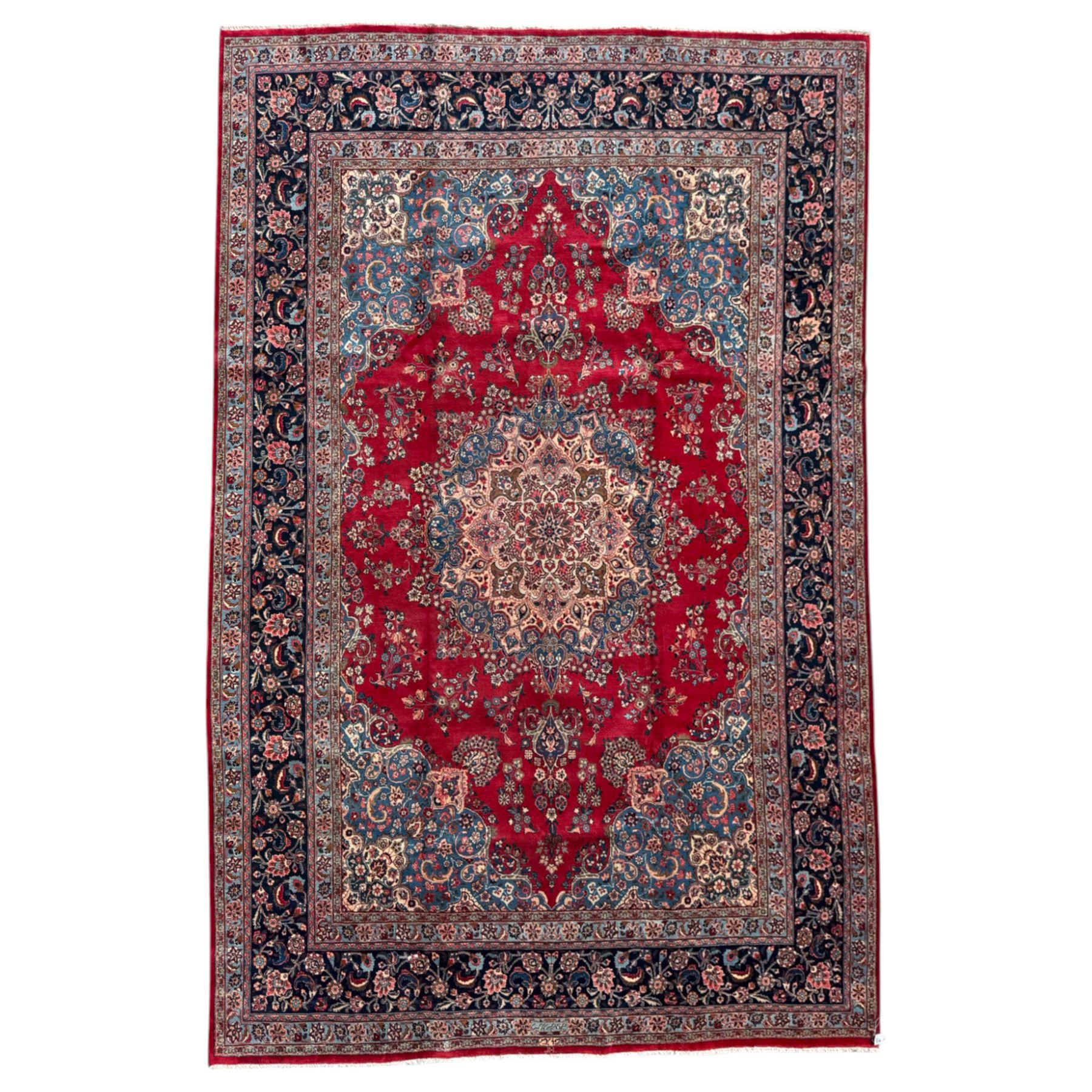 Meshed Persian rug, red, indigo, and teal background with repeating floral vine around a symmetrical floral medallion with bold palmettes, central ivory radiating floral centrepiece, and spandrels, indigo and teal border of delicate scrolling palmette and leafy floral vines