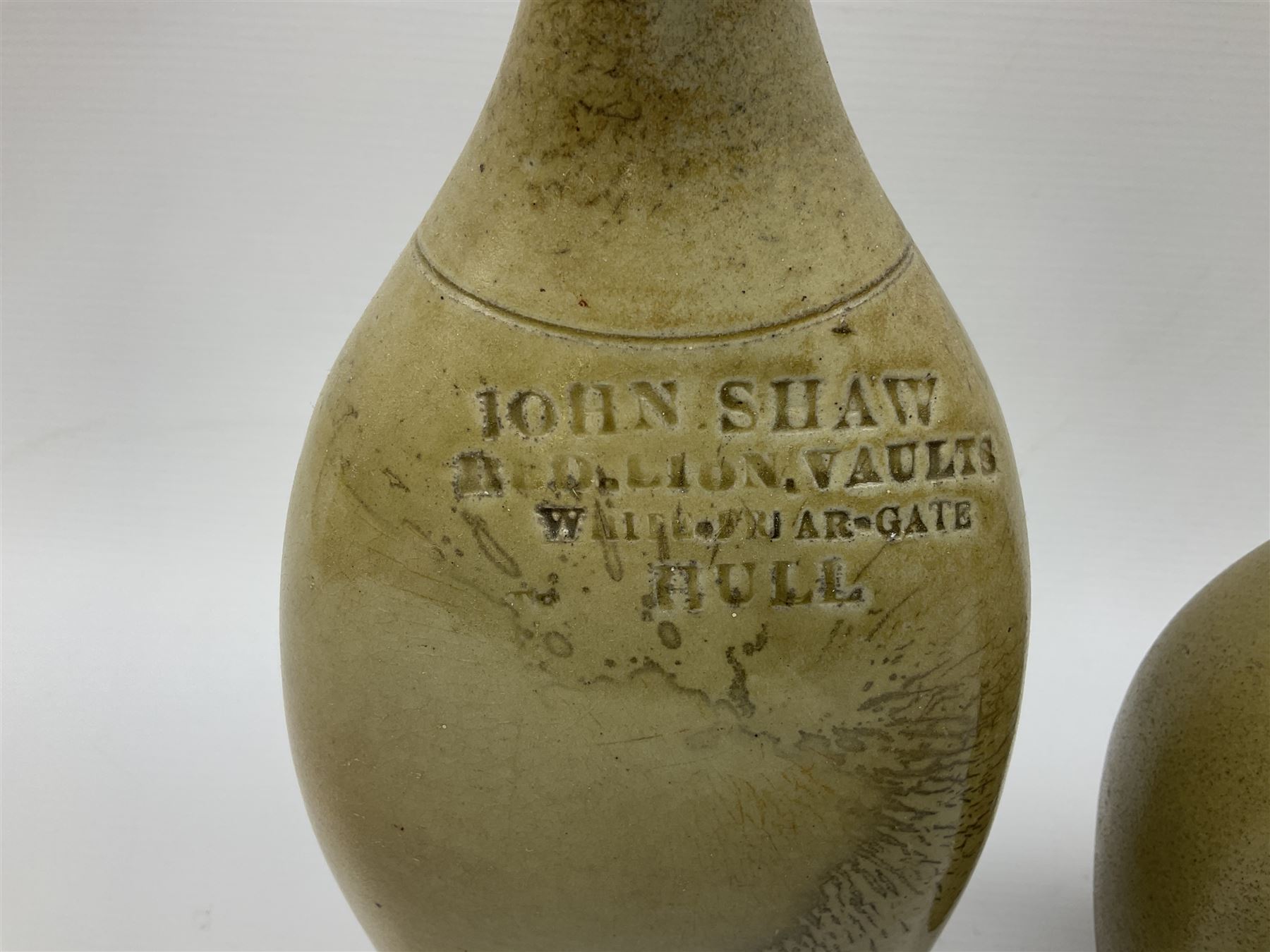  19th century salt glazed stoneware gin bottle impressed John Shaw, Red Lion Vaults, Whitefriargate, Hull of bulbous oval form H27cm and another with impressed label for J. Christie Mytongate Hull (2)  