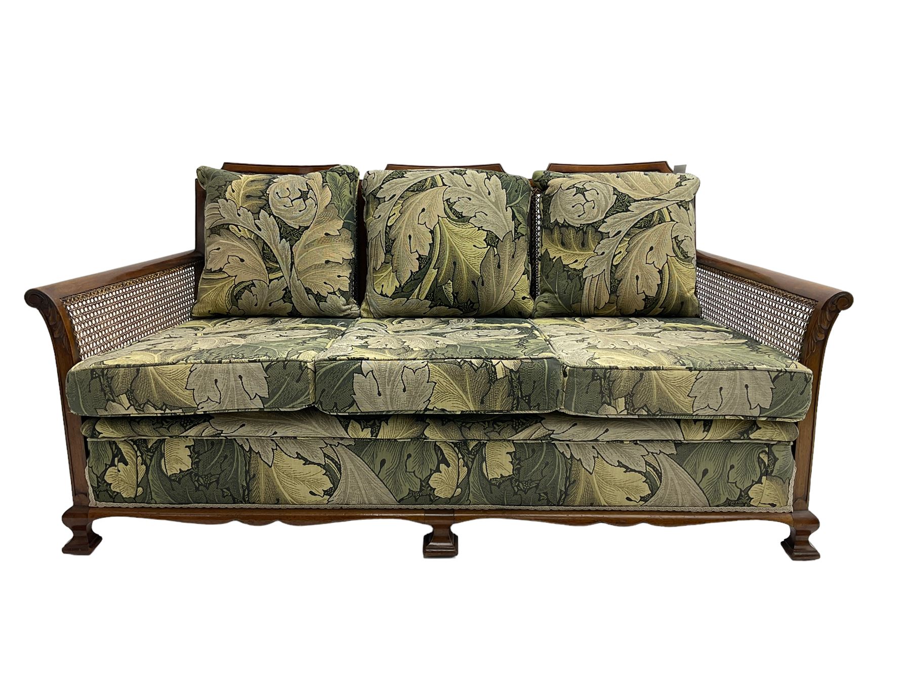 Early 20th century bergère lounge suite, mahogany framed with cane work back and sides, acanthus scroll carved uprights - three seat sofa (W167cm, H82cm, D83cm), and pair matching armchairs (W78cm), loose cushions upholstered in acanthus leaf scroll fabric with scatter cushions