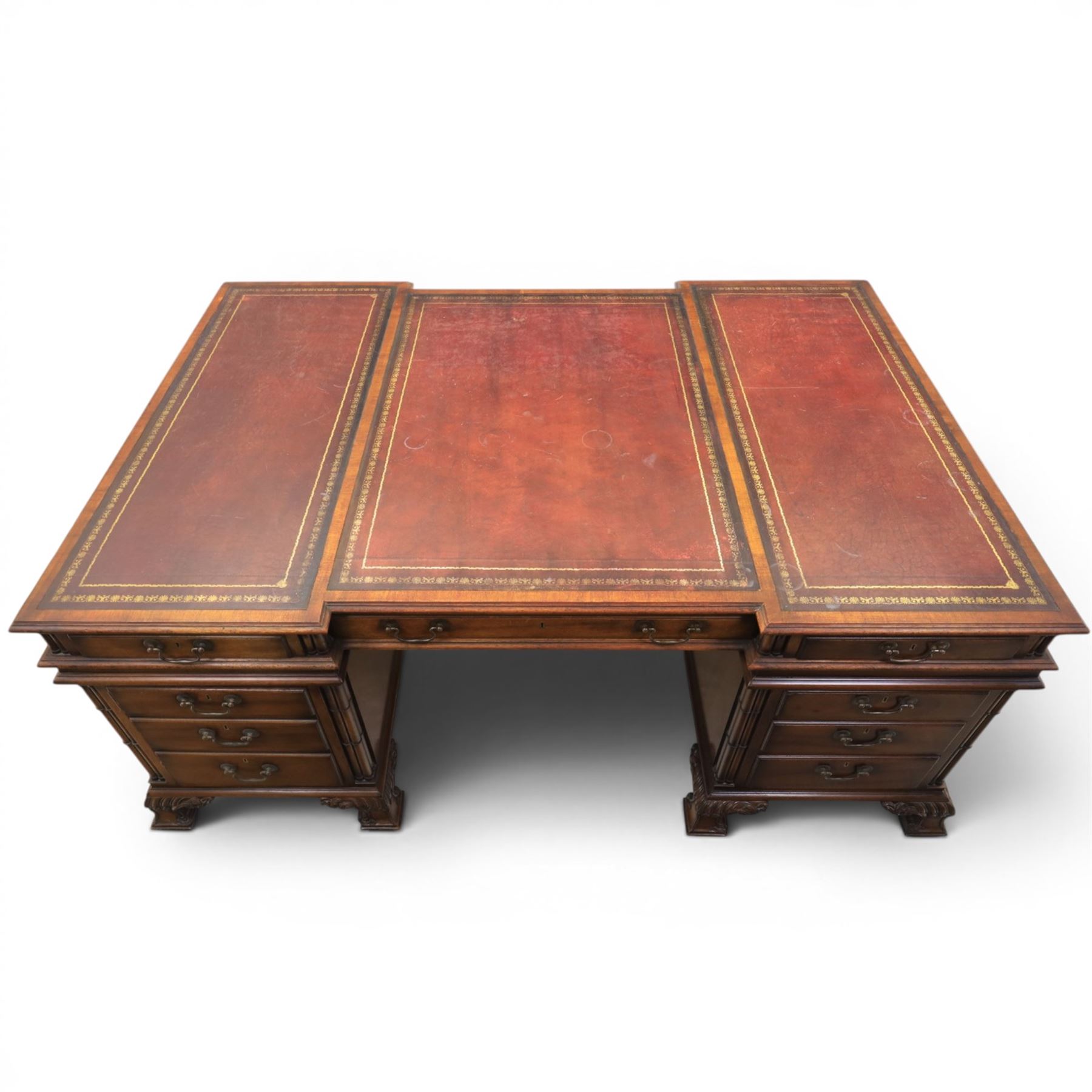 George III style large mahogany reverse breakfront partners desk, red tooled leather writing surfaces crossbanded and moulded edges, flanked by ring-turned cluster columns three frieze drawers with brass swan neck handles, raised on large pedestals with faux drawer fronted cupboard and three graduated drawers, supported on carved ogee feet decorated with C-scrolled and acanthus leaves