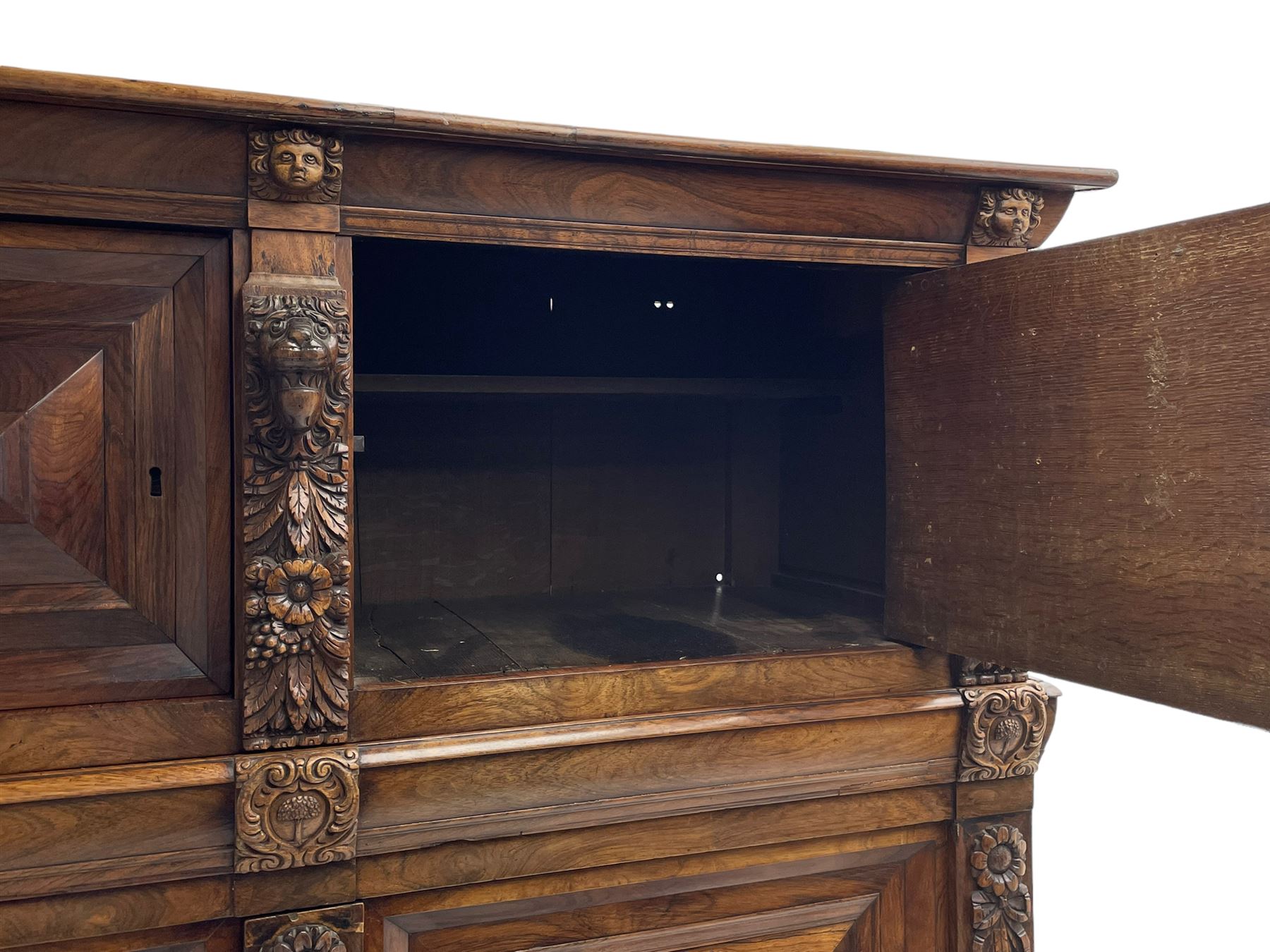 Late 17th century Flemish/Dutch rosewood and oak ‘Zeeuwse Kast’ or cupboard, projecting cornice carved with three putti masks, the uprights carved with lion masks over ribbons, flower heads and foliage, enclosed by four geometric panelled doors, lower central upright carved with flower head over foliate ribbon with bird among foliage, the escutcheon hidden by swivel berry carved cover, interior fitted with shelves, two drawers and shallow hinged cupboard, on two large turned and ebonised feet, circa 1680