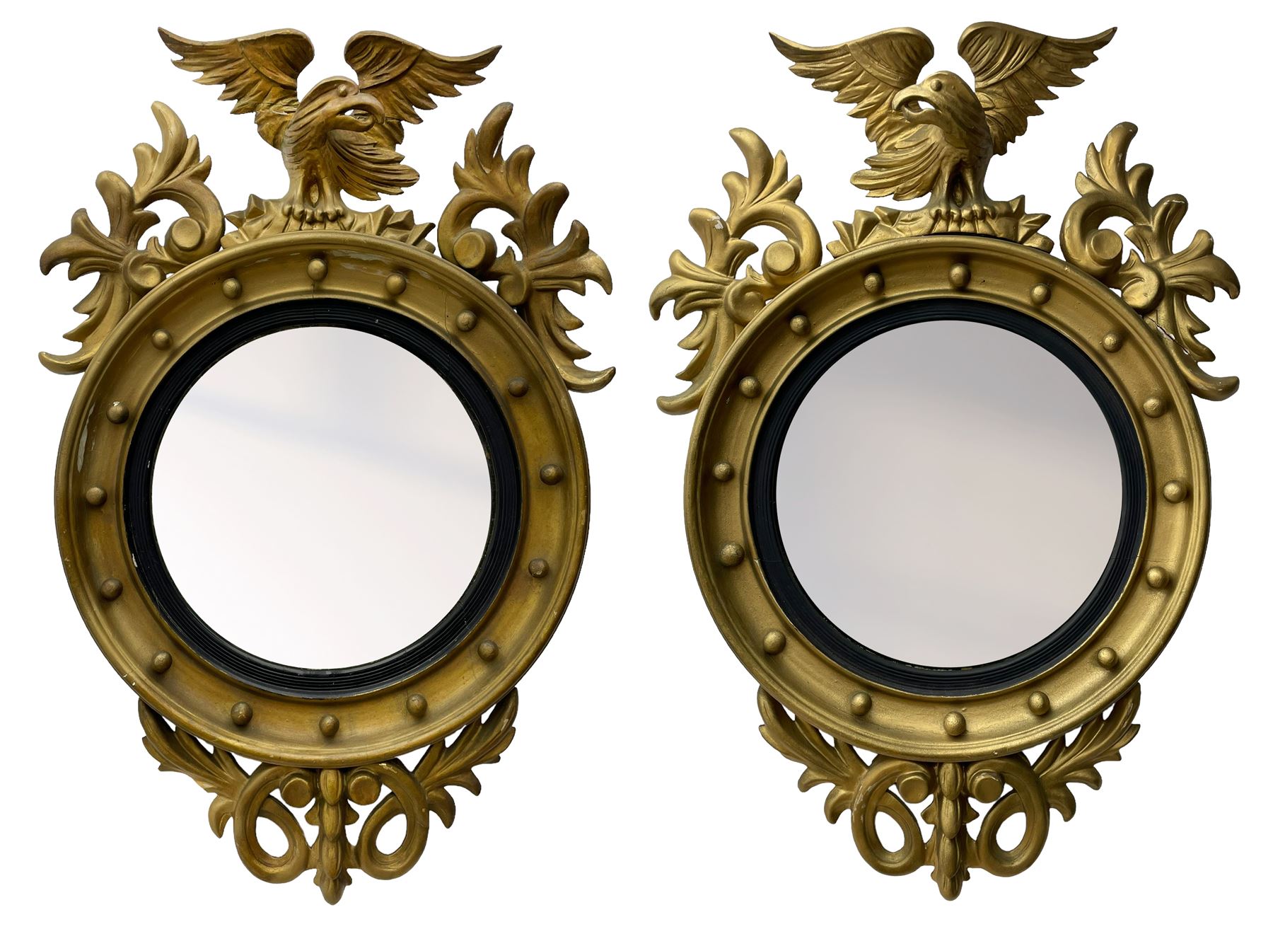 Pair of Regency period giltwood convex wall mirrors, moulded circular frame decorated with spherical mounts surmounted by a carved eagle with spread wings, foliage scroll carved upper and lower brackets, reed moulded and ebonised slip enclosed convex mirror plate 