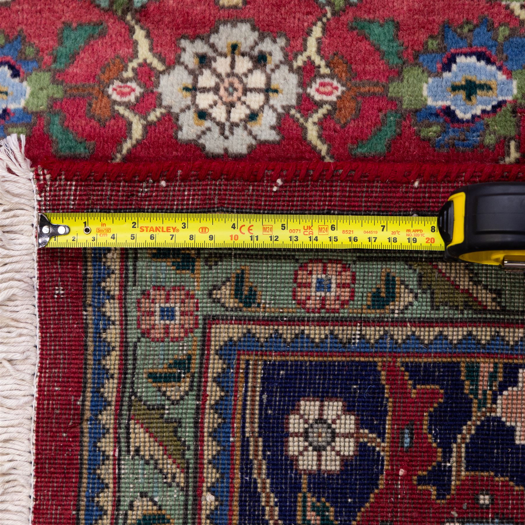 North West Persian Tabriz hand-knotted carpet, herati-type field in deep red with an all-over field densely decorated with scrolling floral sprays and palmettes on a lattice ground enclosed by a dark blue main border filled with stylized floral motifs and interlacing tendrils flanked by multiple guard stripes, with cotton fringe ends 