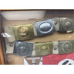 Display of eleven German belt buckles including 'SS', Party Buckle, two Army, Fire Service, two Luftwaffe, NSKK, Hitler Youth and WW1 Army; framed with three cloth badges and an armband
