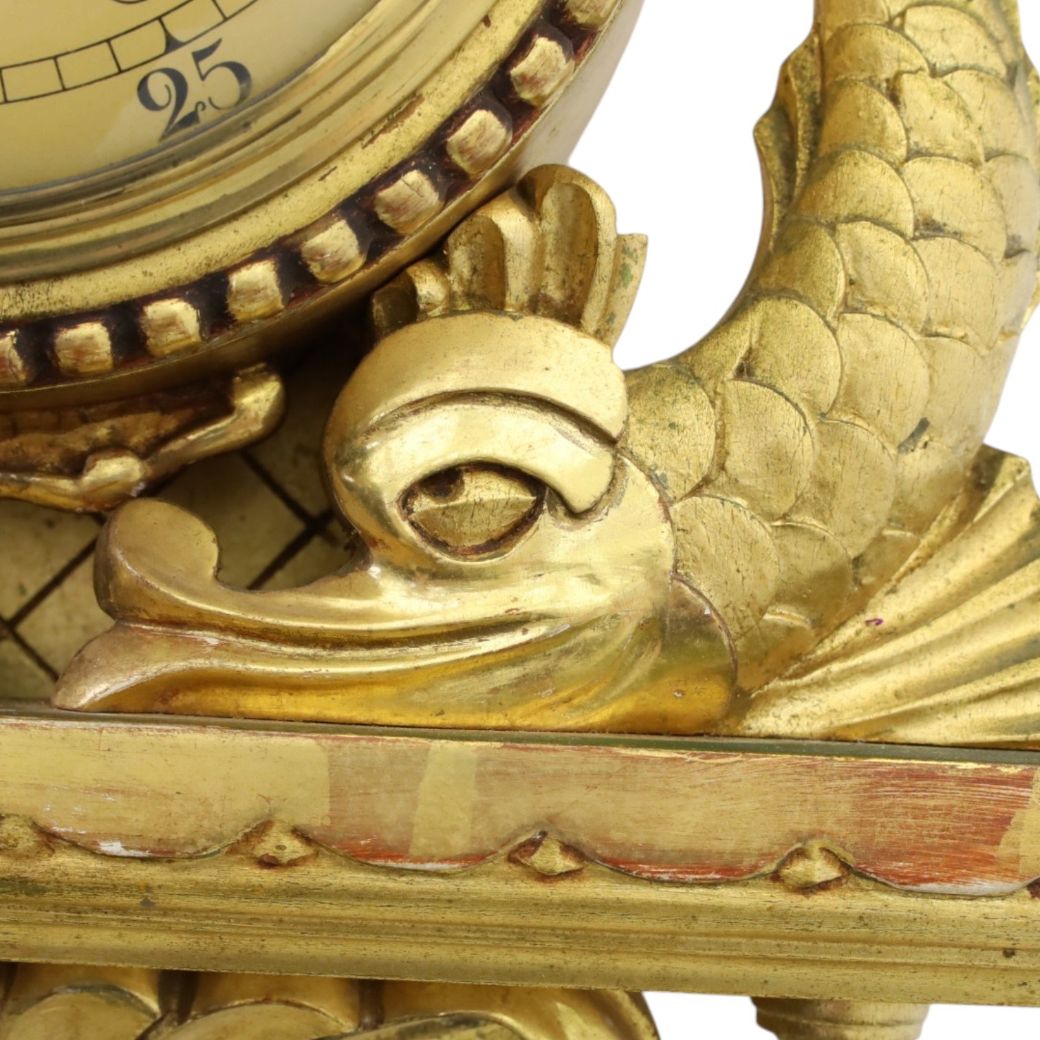 20th century Continental giltwood wall clock, circular dial with Arabic numerals and pierced gilt hands, within a carved case surmounted by a scrolling crest and flanked by stylised dolphins, above a shaped shelf with tassel pendants and a foliate terminal, pendulum missing