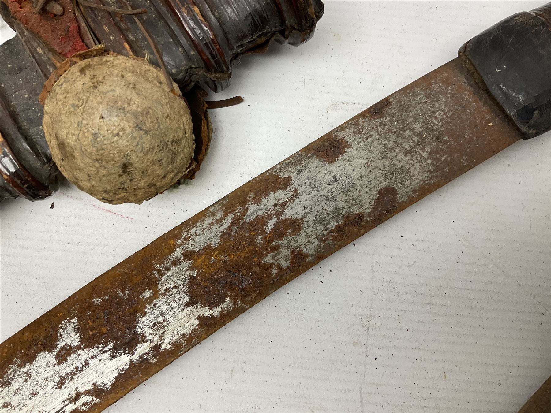 Mandingo sword, the 63cm plain curving steel blade marked with a horses head and the initials G.S.; leather covered grip with metal ribbed spherical pommel; in decorative leather leaf scabbard mounted with tassels and roundels L84cm overall; and a North African flyssa sword in poor condition with wooden scabbard (2)