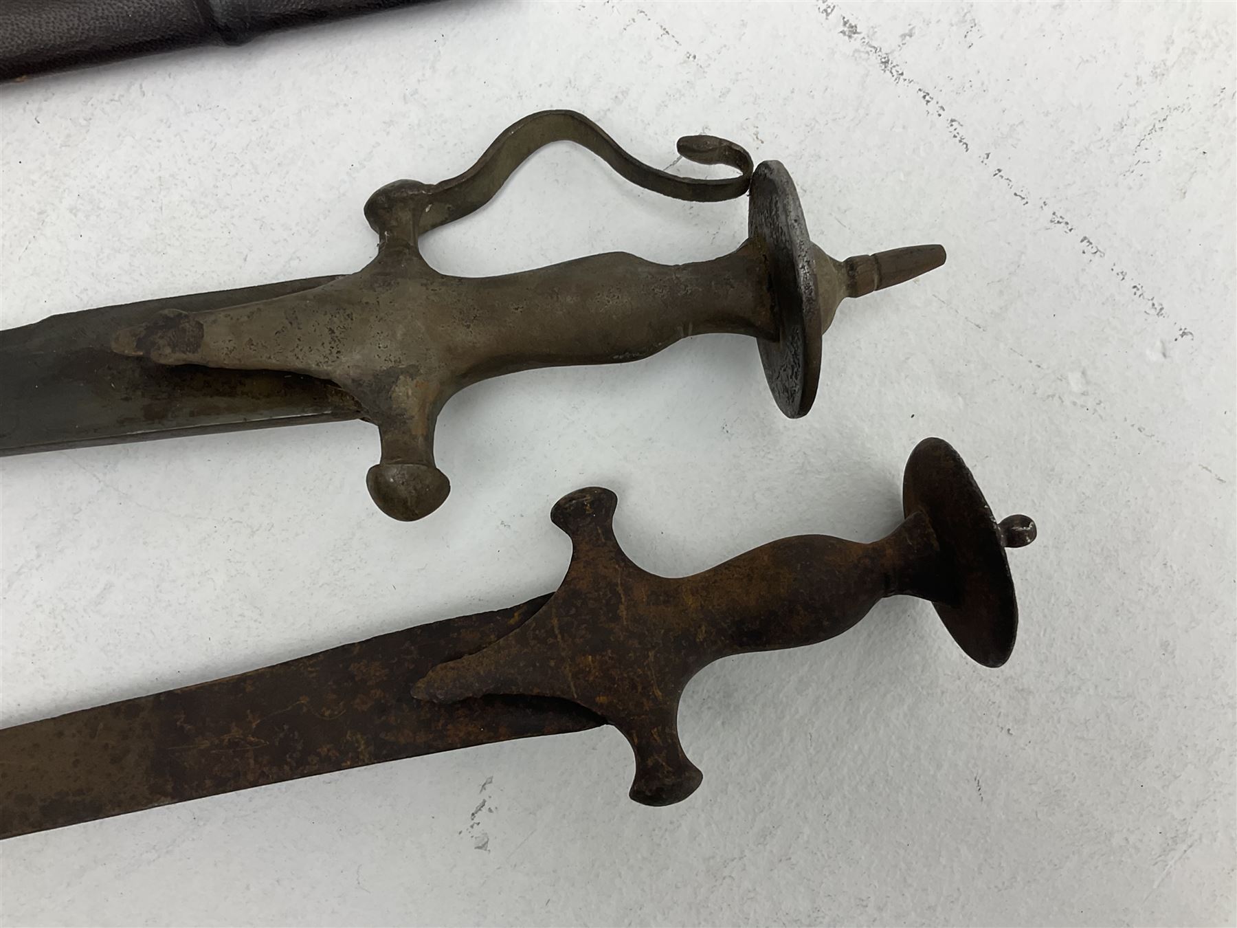 Late 19th/early 20th century Indian Tulwar sword with 81cm plain curving steel blade and iron hilt with extended langets, knucklebow and spiked pommel; in leather covered scabbard L100cm overall; and another Tulwar lacking scabbard in almost relic condition (2)
