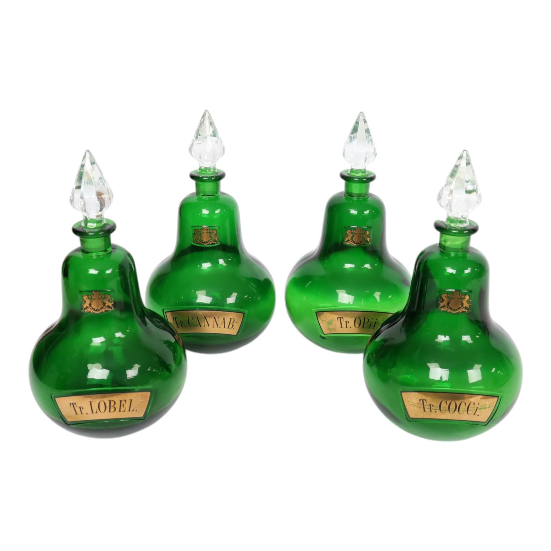 Set of four 20th century Royal Pharmaceutical Society green glass bottles, of bellied form with clear cut glass spire stopper, each body bearing gilt label in Latin: Tr.OPii., Tr.COCCi., Tr.CANNAB., and Tr.LOBEL., and gilt Royal Pharmaceutical Society crest to neck, H25cm

Provenance: From the collection of the family of Peter Green, a practising pharmacist whose career spanned the mid to late 20th century. During his professional life he managed pharmacies in Yeovil, Somerset, and later Selles Chemist in Filey, North Yorkshire, before purchasing and running his own business, Peter Green Pharmacy, located in the Market Place, Malton. The bottles were displayed as part of the traditional shop fittings in both the Filey and Malton pharmacies and were retained as part of his collection.