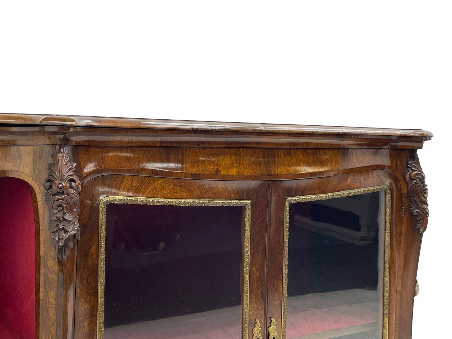 19th century rosewood buffet credenza, bombe form with shaped and moulded top, two central glazed doors with foliate moulded gilt slips, the red fabric-lined interior fitted with a single shelf, flanked by open shelves with raised gilt metal lips, the uprights decorated with shell and flower head carved cartouche mounts, acanthus leaf scroll carved lower mounts, on shaped and moulded plinth base 