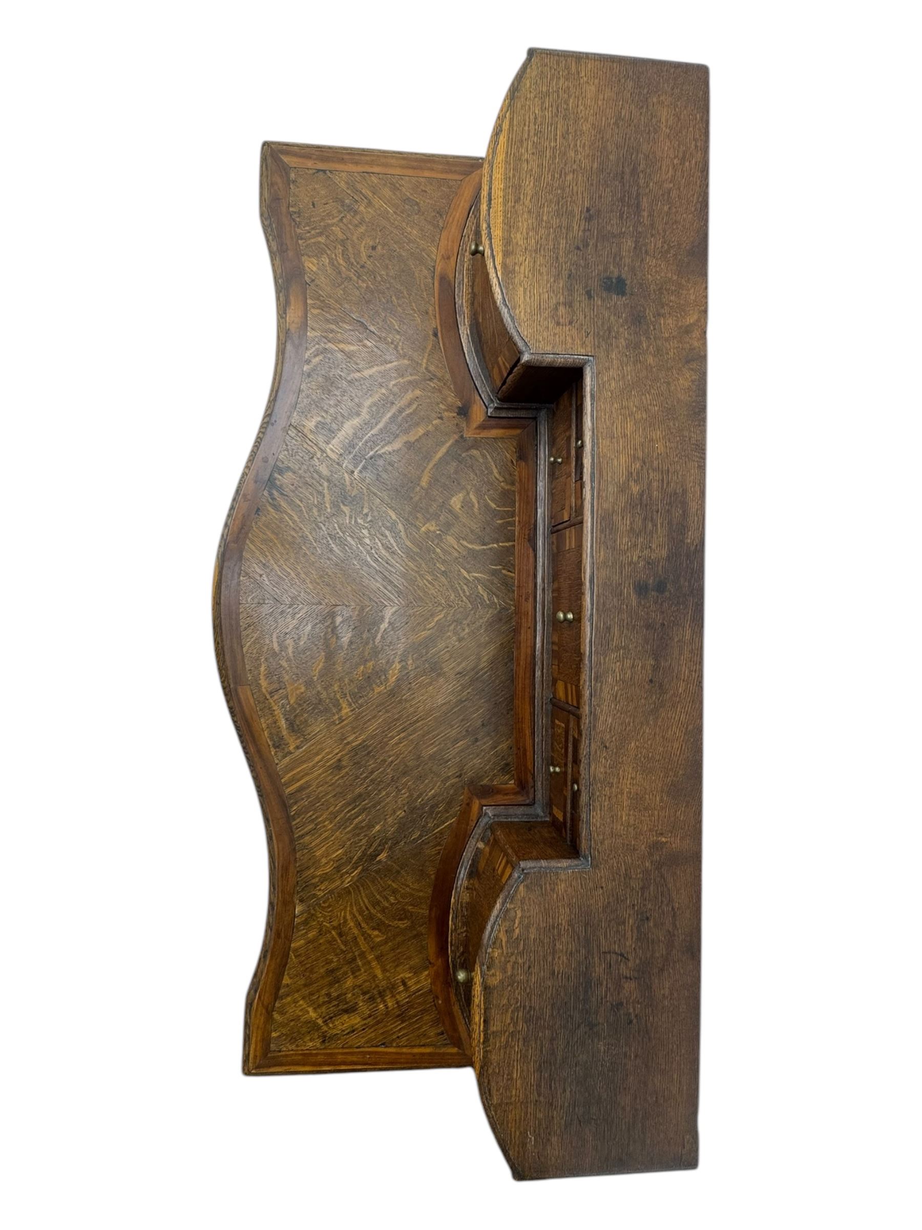 Late 19th century continental oak commode, serpentine fronted with parquetry and crossbanded decoration, the raised superstructure back fitted with a central bank of five recessed drawers flanked by concave drawers, above three full-width drawers with brass ring handles, raised on cabriole supports