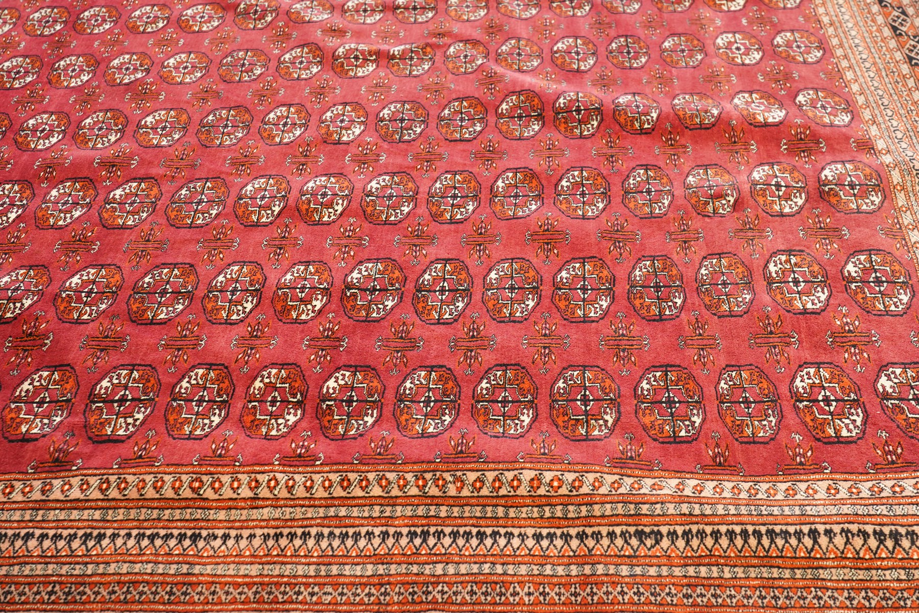 Large Afghan Bokhara crimson ground carpet, the field with rows of repeating Gul motifs and geometric design, enclosed by multiple repeating geometric guard bands
