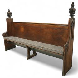 Late 19th century Gothic revival oak church pew, with high backrest framed by carved stylised cross panels and crown-topped finials, shaped end panels with scroll detailing, on block end supports and central stretcher, with later padded seat cushion