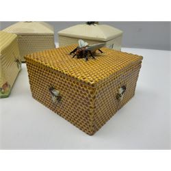Four square honey boxes with lids,  each decorated with honeycomb pattern and finished with a bee finial