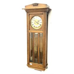 Early 20th century oak cased wall clock, the door glazed with circular convex dial glass and bevelled upright panes, circular brass and silvered Roman dial, twin train driven movement striking on coil 