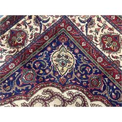Northwest Persian signed Tabriz ivory ground carpet, central medallion with intricate floral motifs, the field and spandrels decorated with scrolling tendrils and palmettes, ivory main border with crimson and indigo floral decorations, surrounded by crimson guard bands