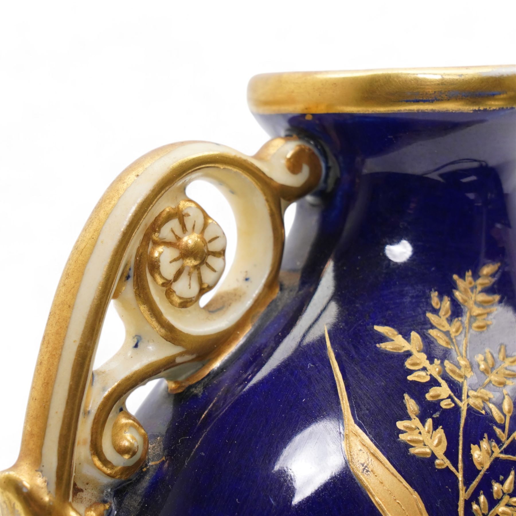 Early 20th century Royal Worcester loving cup, circa 1906, painted with a view of the River Severn and flowers to the reverse, H13cm, Grainger & Co. Worcester twin handled vase, the oval body painted in the Aesthetic style with ferns and grasses in gilt, against a cobalt blue ground, with scrolled handles and quatrefoil foot, H17cm (2)