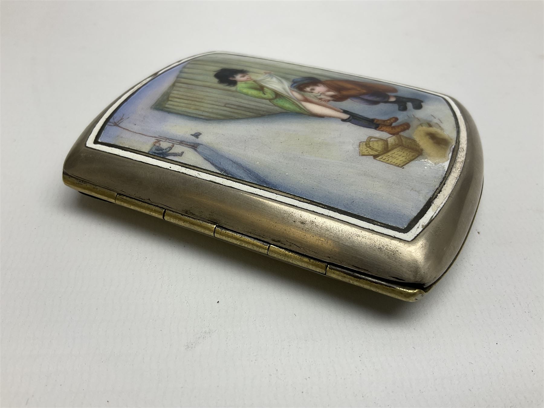 Early 20th century Continental erotic cigarette case, the silver-plate body of curved rectangular form with cover decorated with painted enamel street scene depicting young boy in squatting position lighting a cigarette shielded from the wind by his girlfriend, who is lifting the skirt of her dress up over him, with gilt interior, L9cm