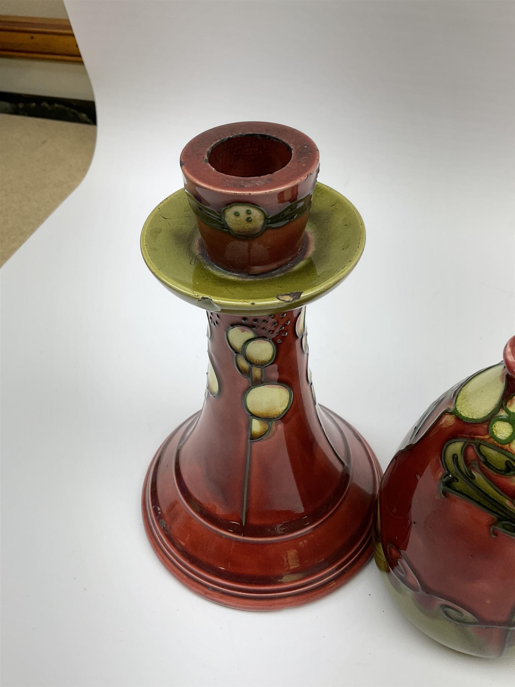 Minton Secessionist vase, with tube-lined stylised flower head decoration upon a red and green ground, printed mark to base 'Minton Ltd, No. 31', together with a matching pair of Minton Secessionist candle sticks, candlestick H17cm