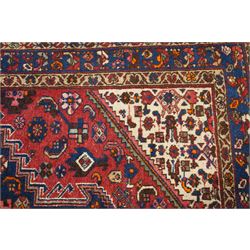 Persian Heriz crimson ground carpet, the central navy geometric medallion on a red crimson ground field, surrounded by further geometric stylised motifs and foliate designs, enclosed by multiple guard-lines  
