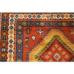Caucasian Kazak vermillion ground rug, the sectioned field decorated with three geometric lozenge medallions surrounded by stylised plant and animal motifs, the multiple guard bands with repeating geometric design