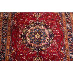 Persian Kashan hand-knotted rug, madder red ground centred by circular floral medallion with pendants, surrounded by scrolling vines, palmettes and flowerheads, dark navy spandrels, enclosed by dark navy floral border with multiple guard stripes