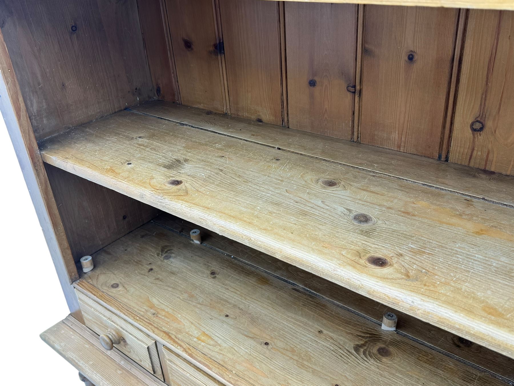 Early 20th century pine kitchen dresser, featuring a hutch with arched top over three open shelves, the base with five drawers over three cupboard doors, turned column supports flanking the doors, scalloped apron base with bracket feet