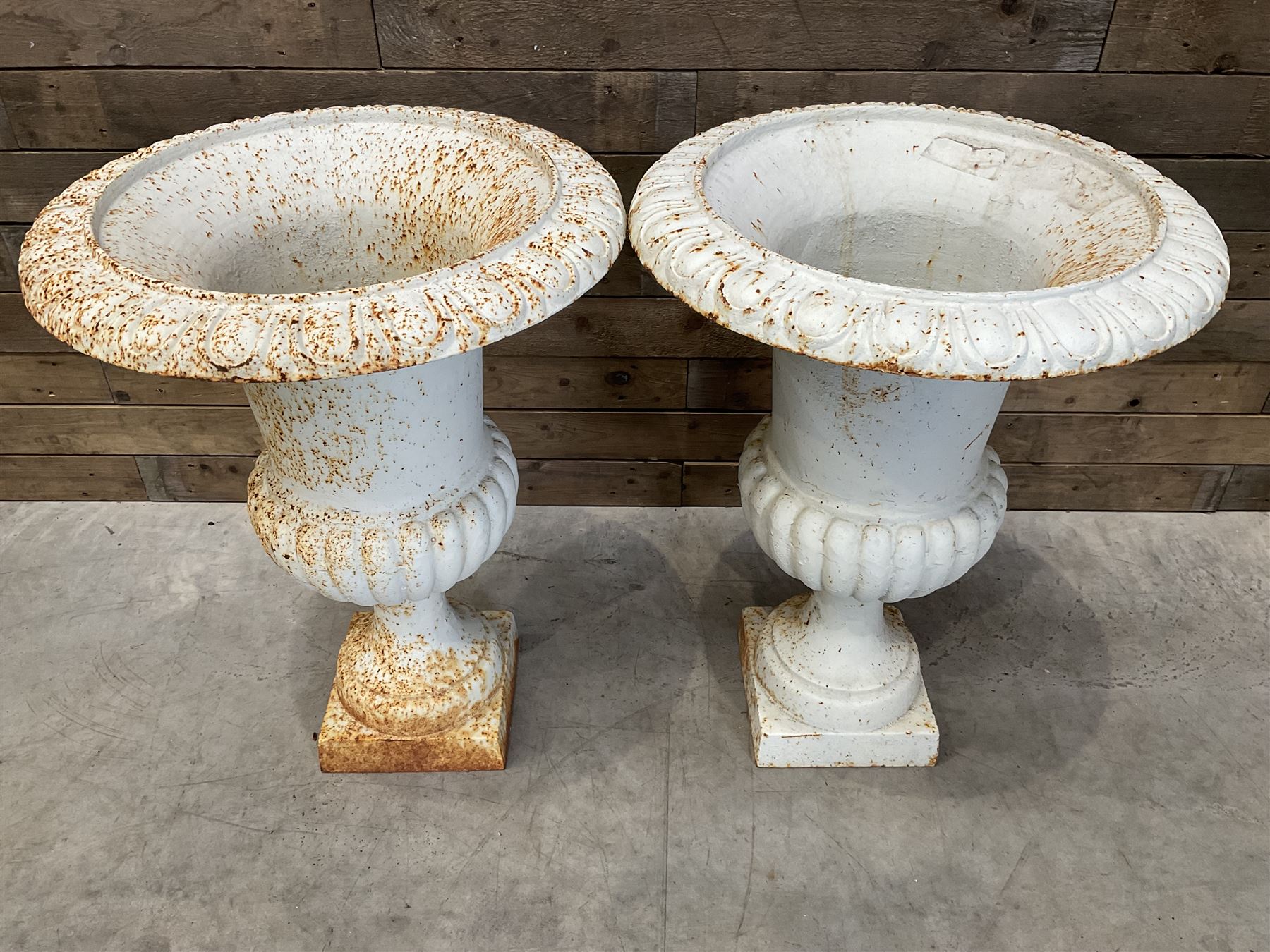 Pair of large Victorian design white painted cast iron campana shaped garden urns, egg and dart rim over a gadrooned underlobe, tapering column on square plinth base
