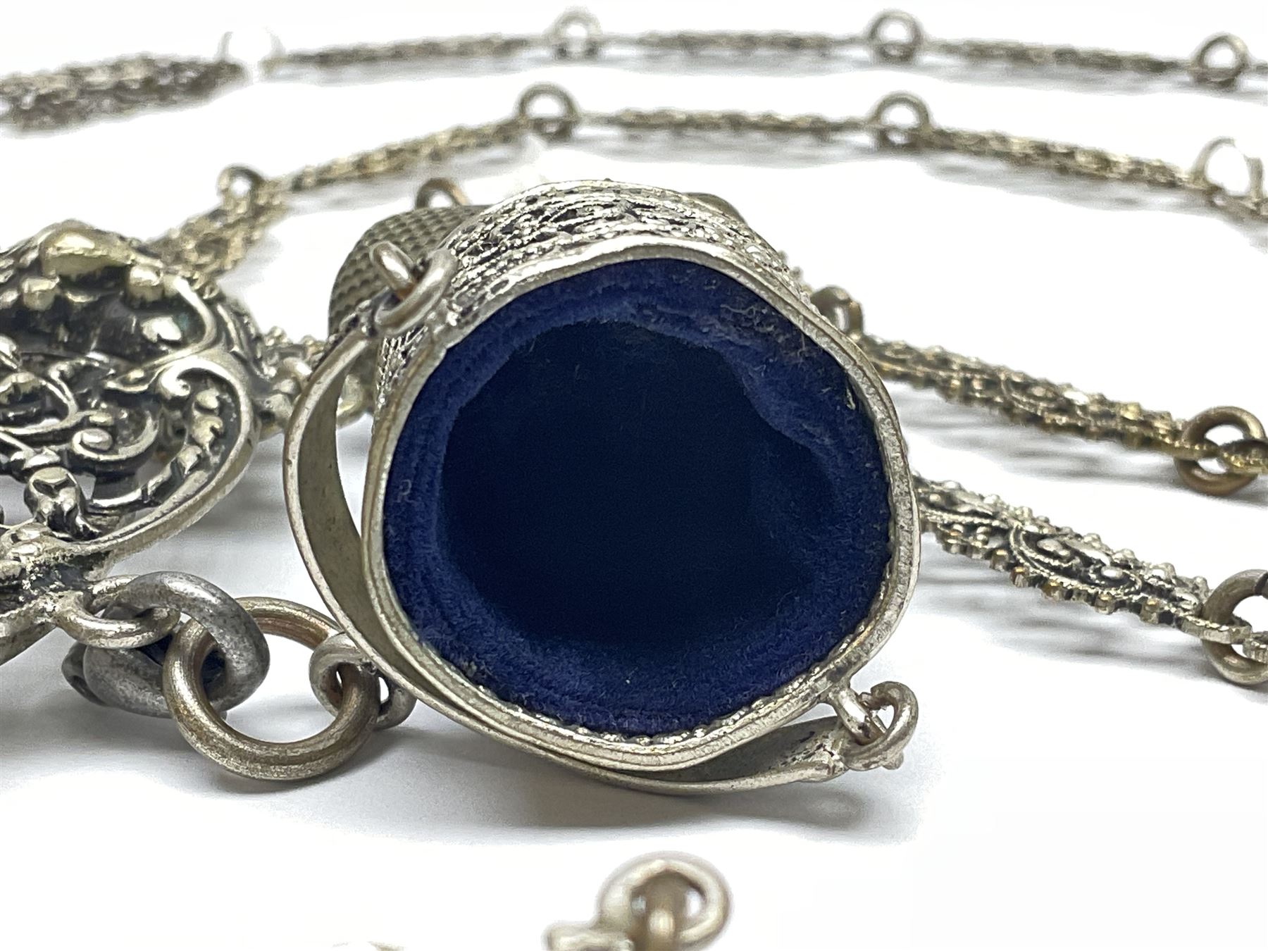 19th century continental silver plated chatelaine, the main body flanked with winged mythical beasts and central soldier slaying a dragon supporting three suspended items to include velvet lined small basket and long clasped filigree chain, together with a thimble