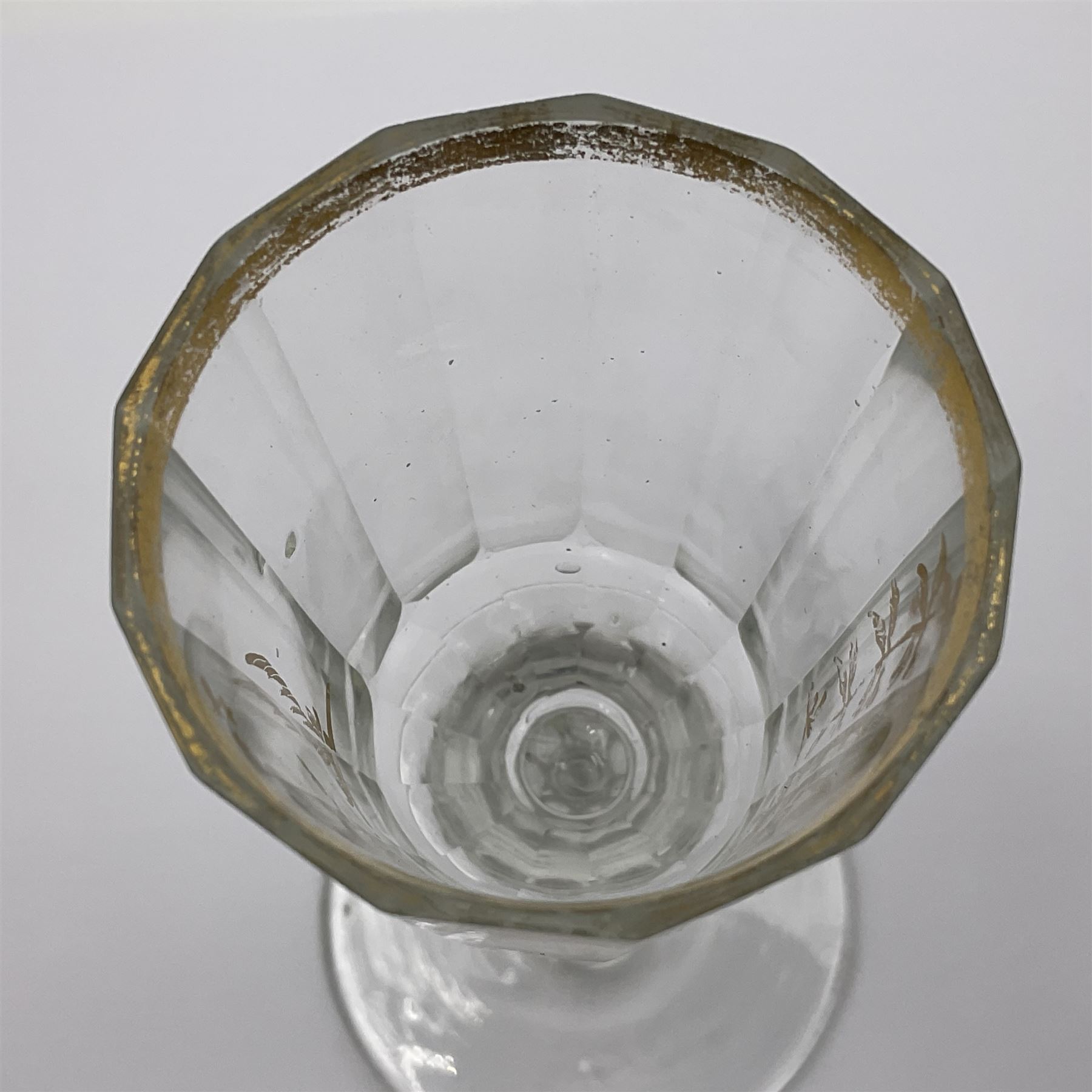 Three 18th century wine glasses comprising a plain stemmed glass with bell shaped bowl and conical folded foot H16cm, another plain stemmed glass with ogee bowl and folded foot and a Continental glass with gilt faceted bowl, decorated with male figure within a landscape, on a clear Silesian seven sided cut stem (3)