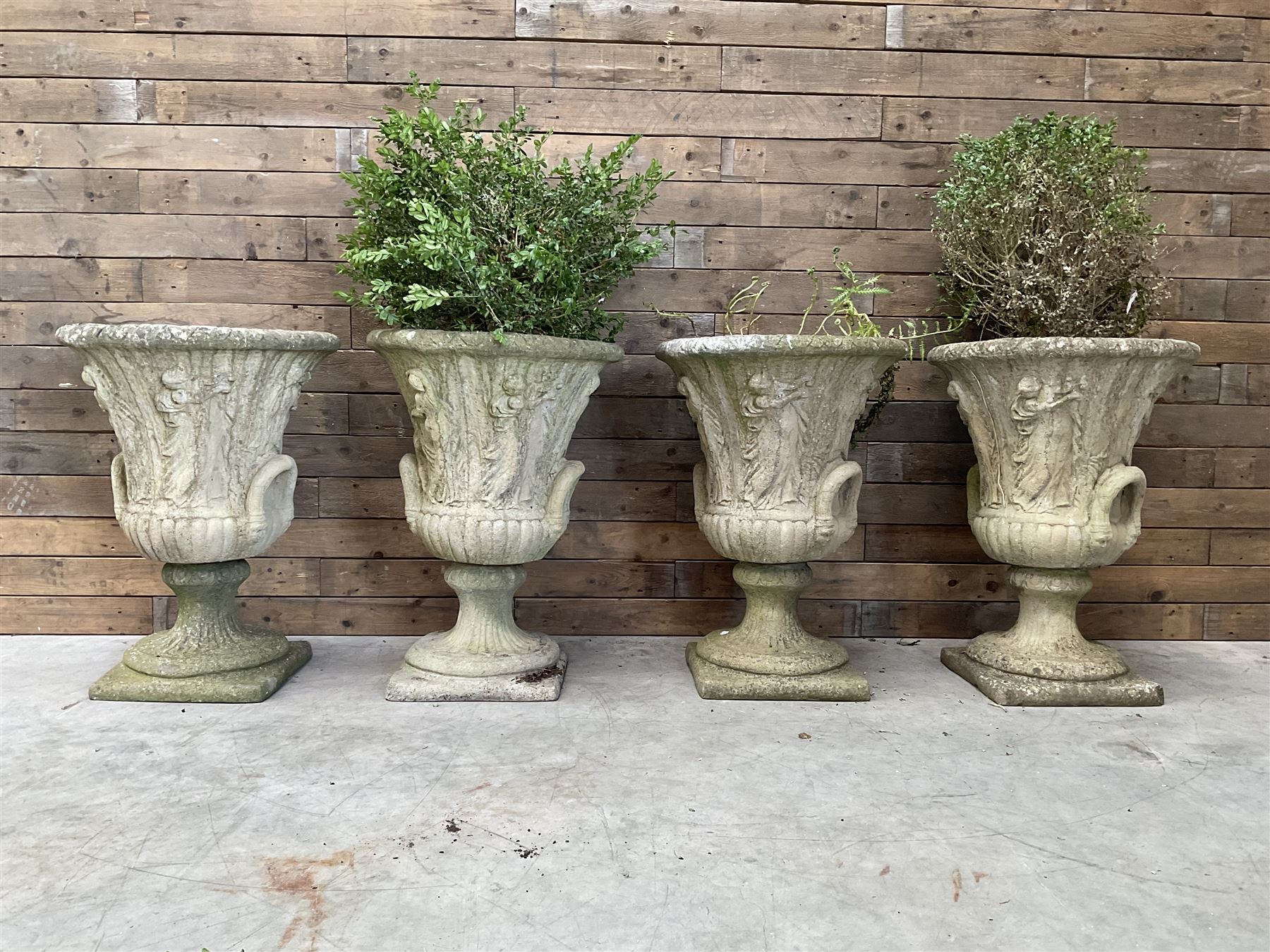 Set of four Victorian design cast stone Grecian urns, tapering form cast with figures and handles, square plinth bases
