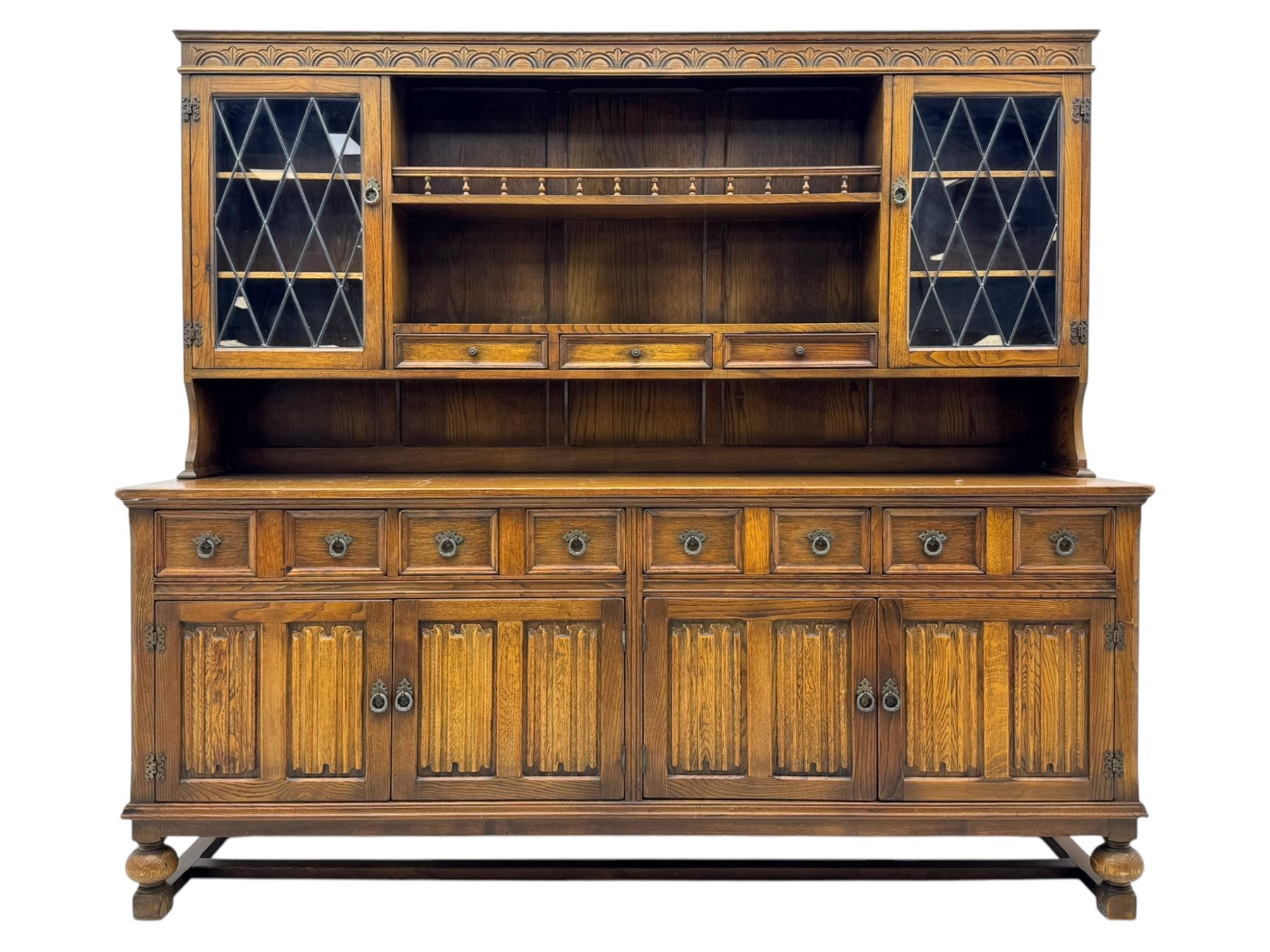Large mid-20th-century oak dresser with two astragal glazed doors between gallery shelf and lower shelf, with three short drawers and lower section with four drawers and three double-panelled linen-fold hinged cupboard doors 