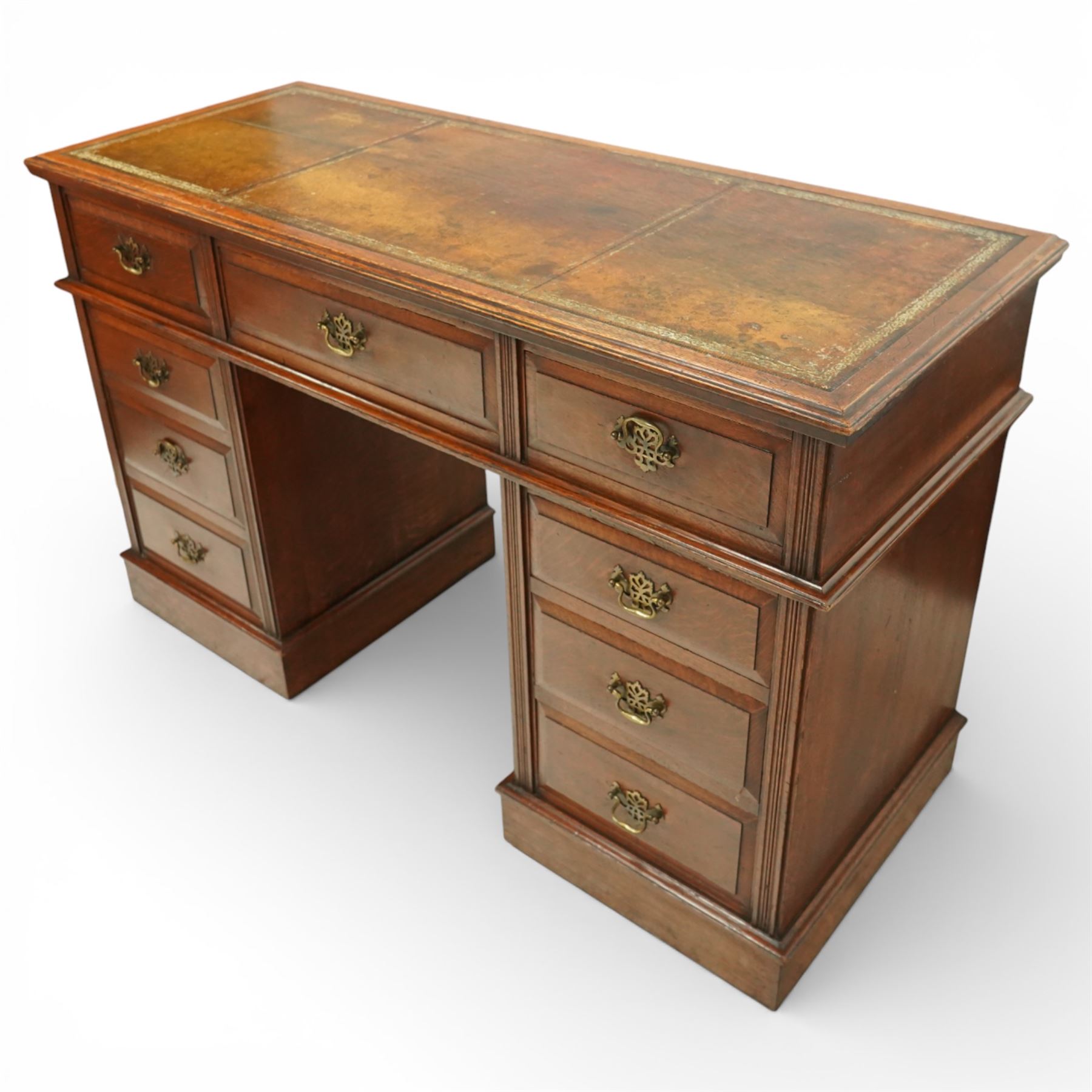 Late Victorian oak nine drawer desk, the rectangular top inset with a tooled leather writing surface bordered in gilt, above three frieze drawers and two pedestal cupboards each fitted with three graduated drawers, all with brass swan neck handles, raised on plinth bases