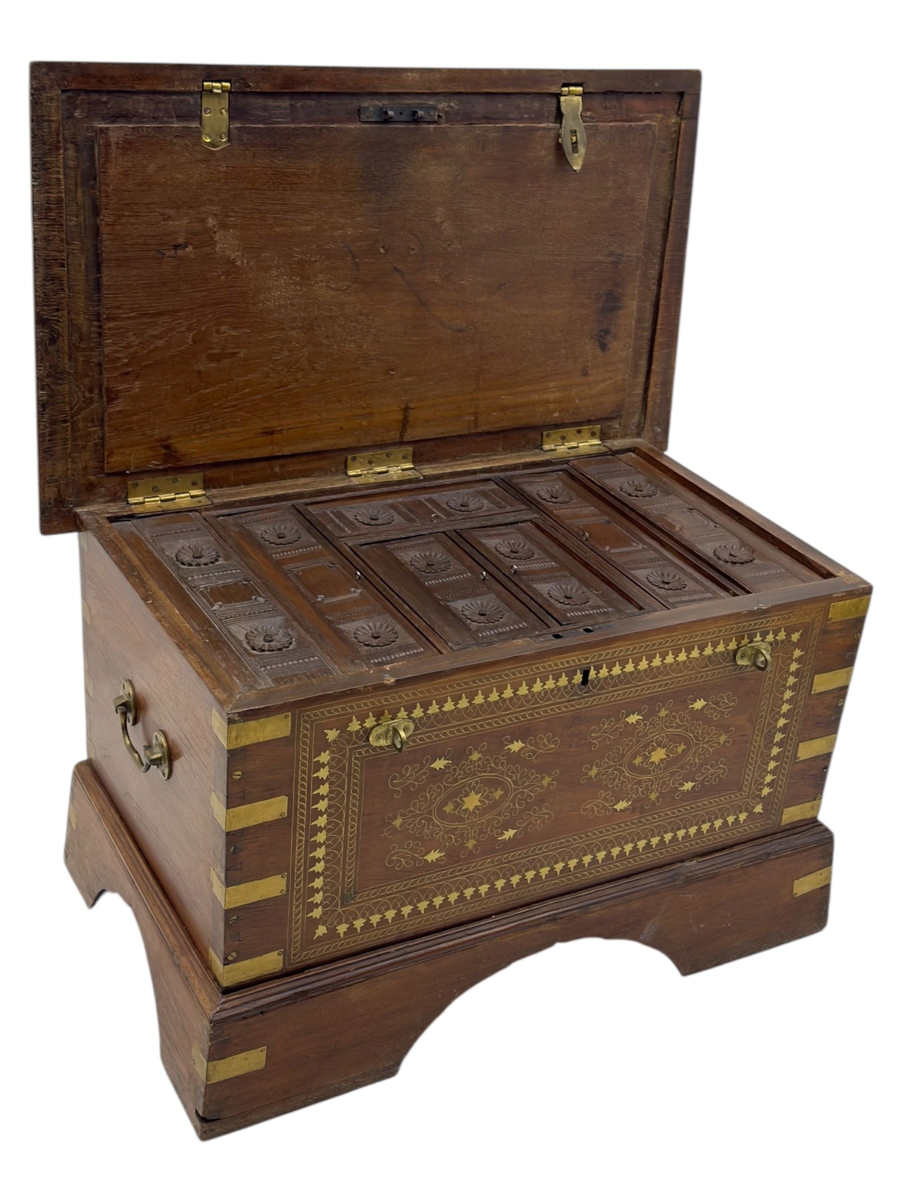 Zanzibar chest, early 20th century, of hardwood construction with brass inlaid foliate and geometric decoration to the lid, fitted interior of multiple carved compartments, with brass strapwork, side handles, and shaped bracket feet