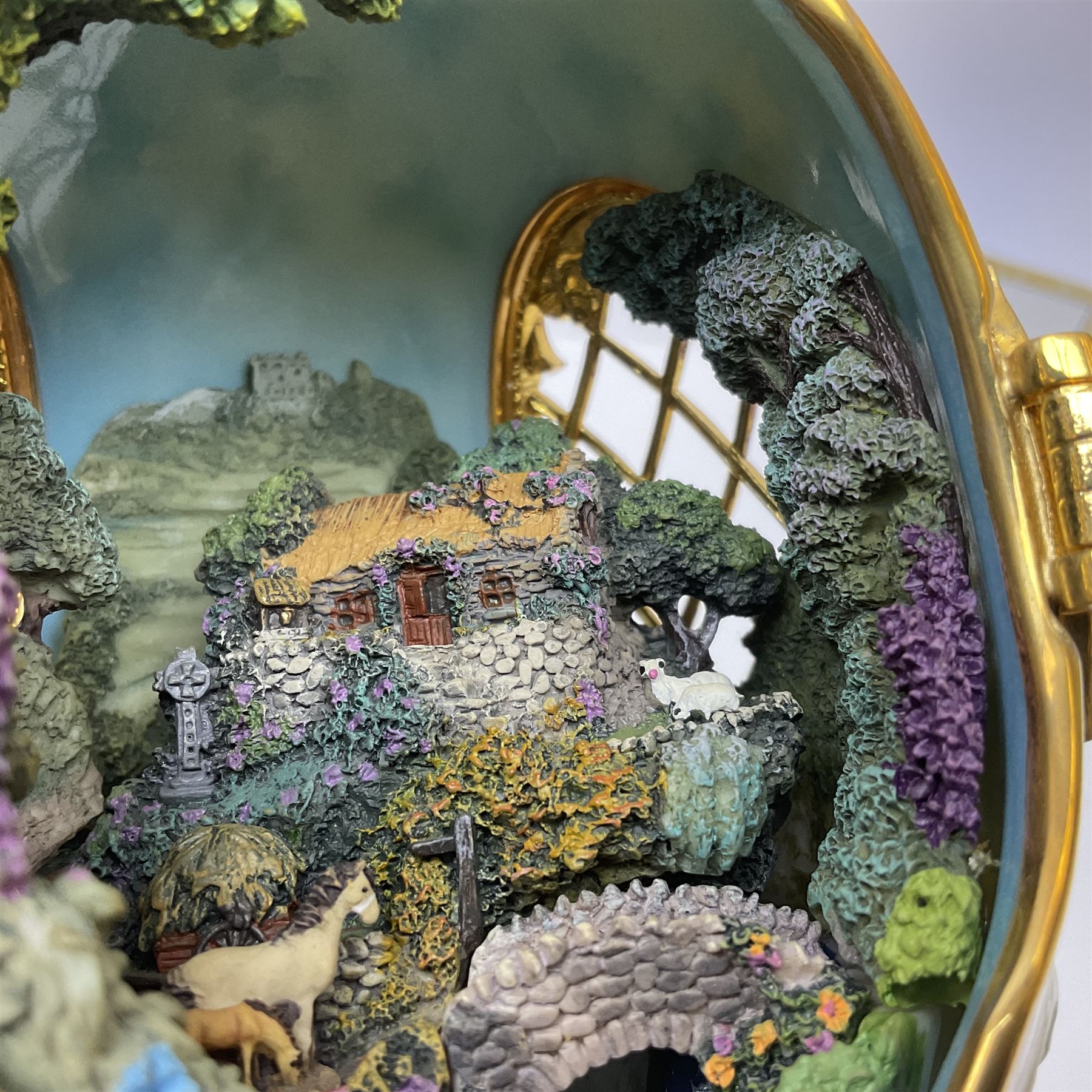 Franklin Mint The Emerald Isle Collector Egg, the egg decorated with embossed shamrocks upon a cream ground, with a gilded shamrock finial, accents and openwork door, opening to reveal a miniature landscape scene, upon three gilded feet set with green paste stones, with certificate of authenticity H23cm, 