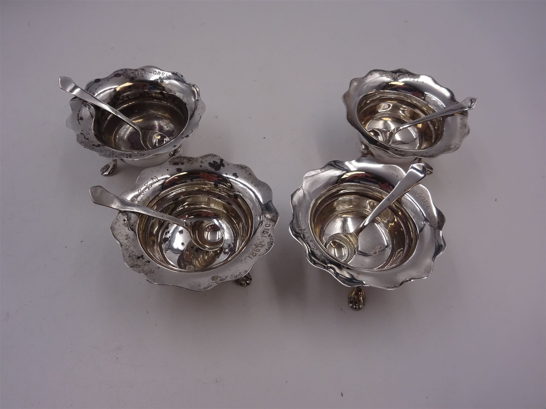 Set of four Edwardian silver open salts, of circular form, each with later personal engraving to scalloped rim and upon three pad feet, together with four matching silver salt spoons, hallmarked James Deakin & Sons, Sheffield 1909, in velvet and silk lined fitted case     
