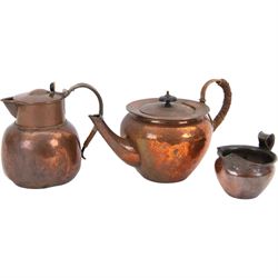 Keswick School of Industrial Arts: Arts & Crafts copper teapot, of stylised squat form with cane bound reed handle and ebony finial, together with a lidded jug, of bellied form with cane bound handle and Bakelite type thumbpiece and a cream jug of squat form with stylised loop handle, all stamped KSIA beneath, tallest H14cm