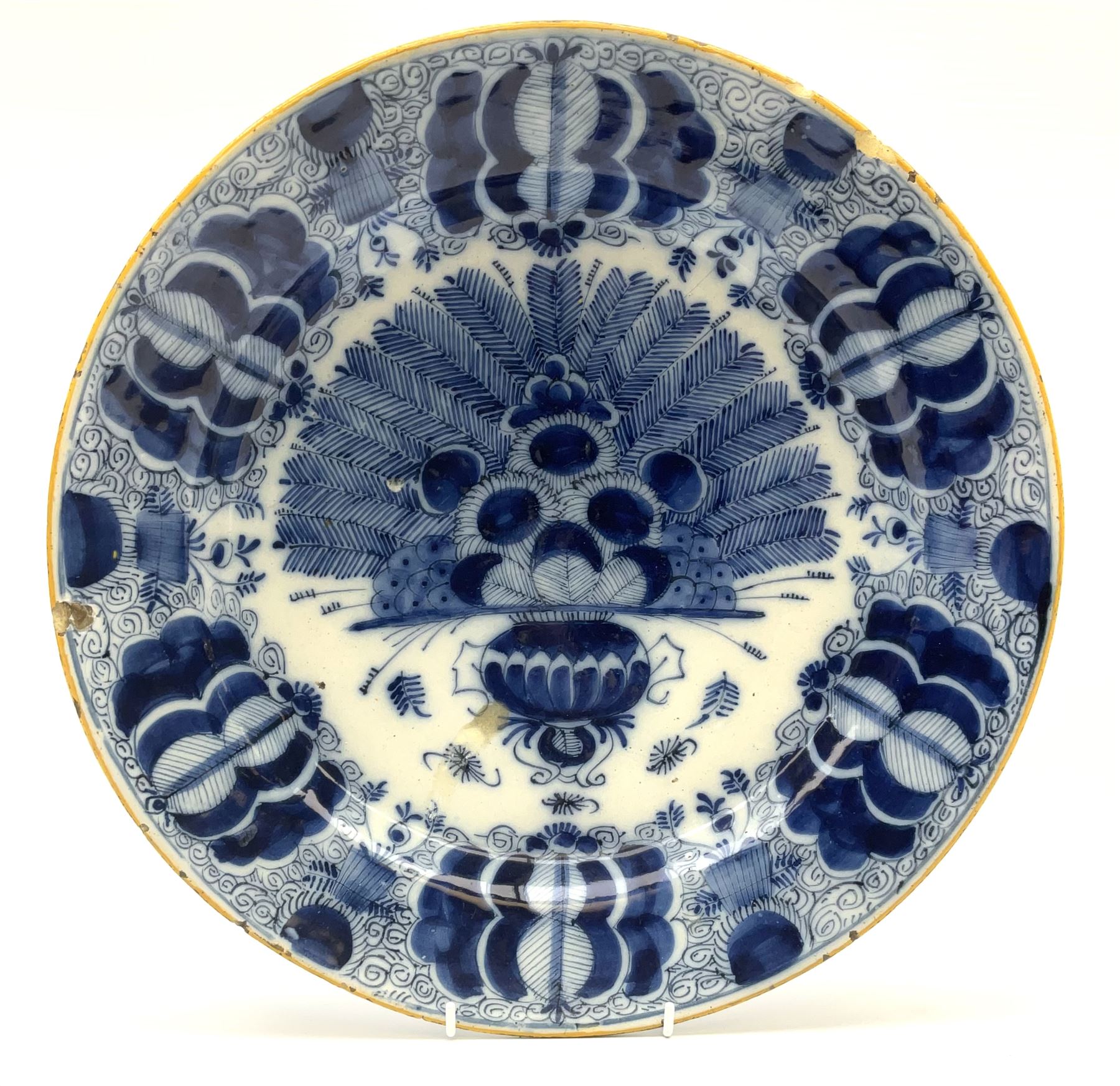 18th century Delft blue and white peacock pattern dish, painted with a fan of peacock feathers behind an urn of fruit and flowers, D34.5cm. 