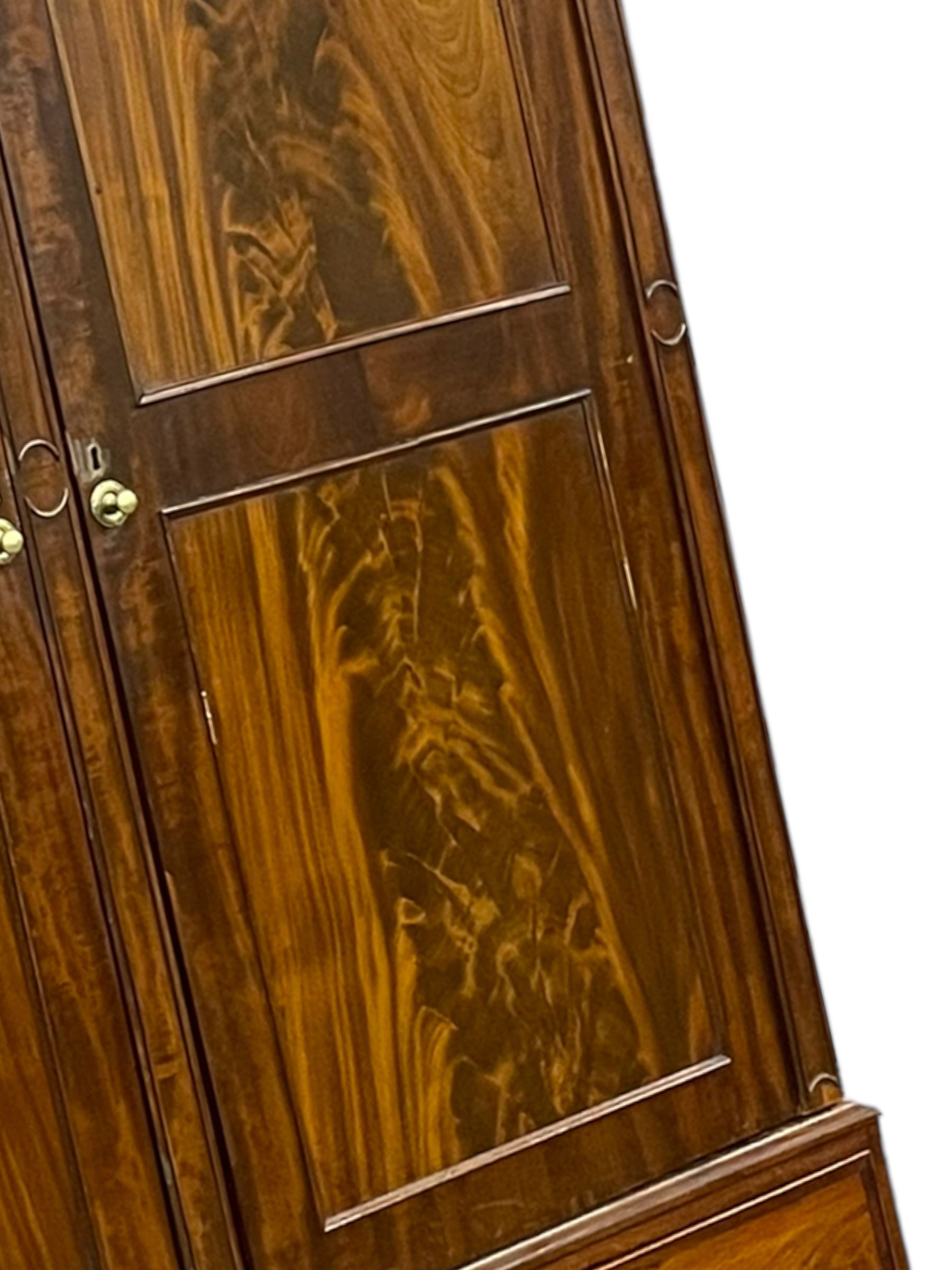 George III mahogany double wardrobe, the projecting cornice with dentil moulding over two panelled doors with mirror-lined interiors, enclosing hanging rails and brass hooks, the base fitted with two drawers, raised on bracket feet