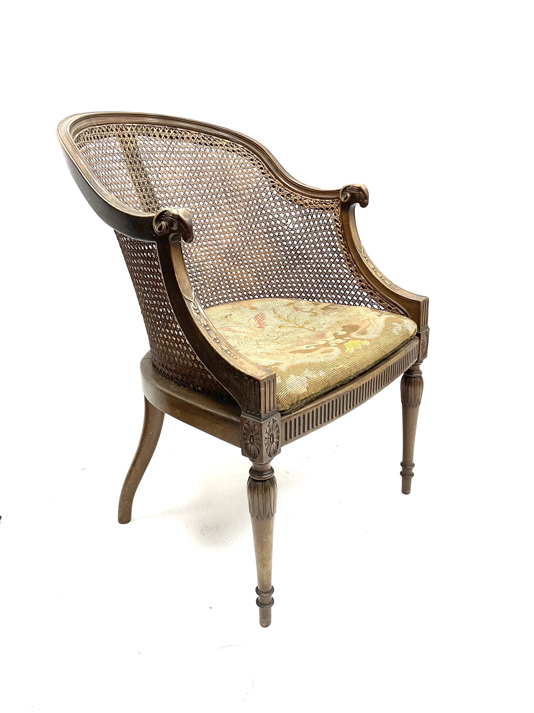 Early 20th century walnut Bergère chair, moulded and shaped frame terminating in rams head, cane woven back meets patterned upholstered seat, raised on leaf carved and fluted supports 