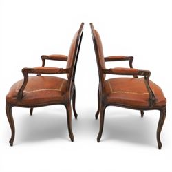 Pair of late 20th century French style carved beech open armchairs, the shaped and moulded frames with foliate cresting rail above padded backs and overstuffed seats upholstered in tan leather with gilt foliate borders and close nailed trim, raised upon cabriole supports with acanthus carved knees