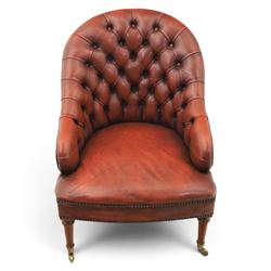 Victorian style oxblood leather armchair, deep button upholstered back and sides with rolled arms and brass studded borders, on turned front legs with brass and ceramic castors and splayed rear supports