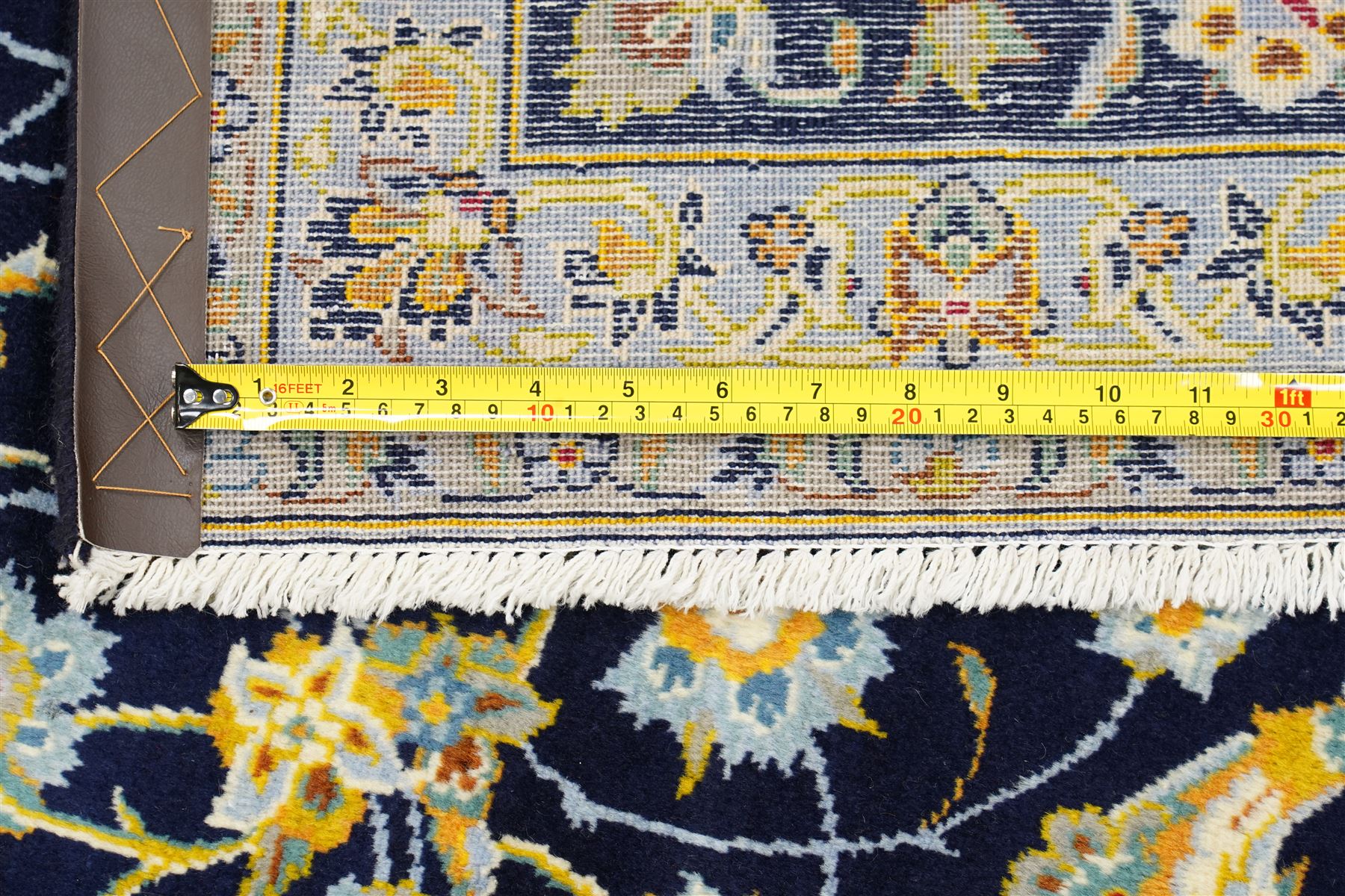 Central Persian Kashan hand-knotted carpet, deep indigo field with a densely all-over arrangement of scrolling floral vines, palmettes, and flowering sprays, in soft ivory, pale blue, and warm gold tones, principal ivory border with a continuous meandering vine of stylized palmettes, and floral motifs, flanked by multiple narrow guard borders, with cotton fringe ends 