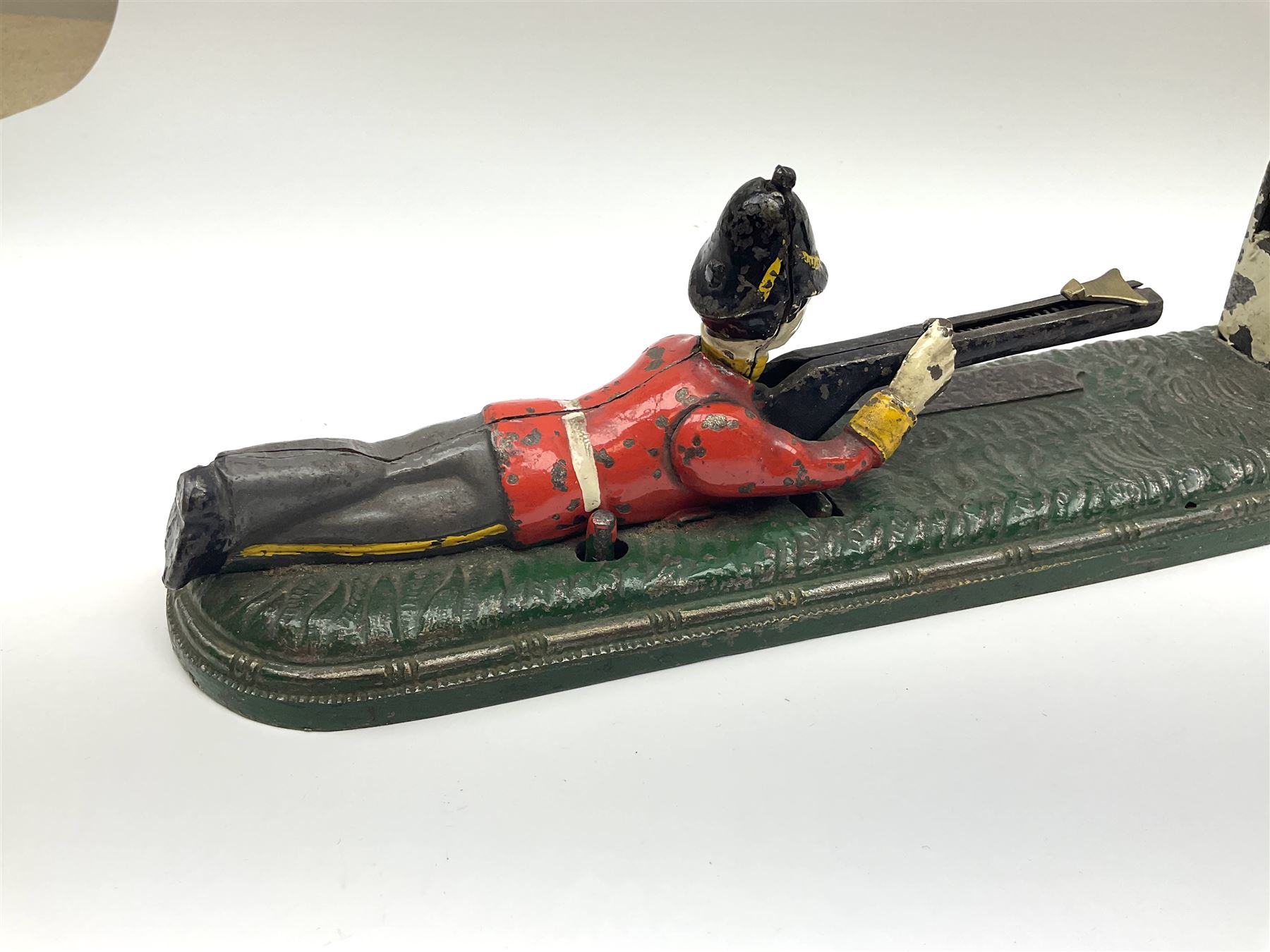 Very rare 19th century John Harper & Co. mechanical cast-iron money box, registered number 33821 patented 1885, inscribed on metal plaque 'Wimbledon Bank', based on the Queen's Trophy for shooting at Wimbledon, depicting a British Infantry man in red tunic and blue trousers lying on the ground using a gun to fire a brass coin launcher into a pill box with removable moving flag above L30cm