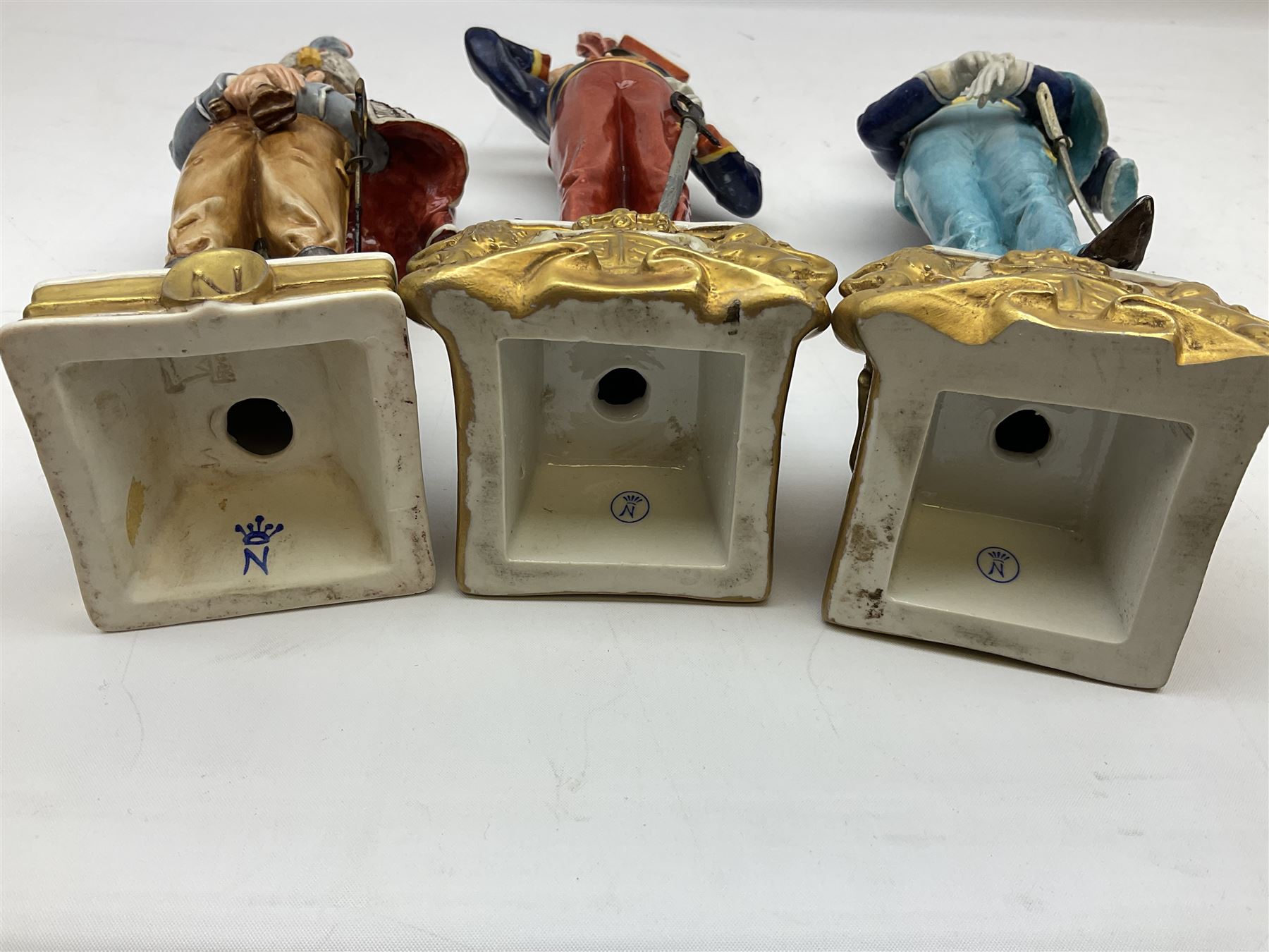 Group of seven Capodimonte figures of soldiers, to include four Bruno-Merli examples including Officer of the 12th Lancers 1820 and Captain of the 18th Hussars 1815, both raised upon ornate gilt plinths bearing British monarch motto in Latin 'Dieu et mon droit', and three further similar, all with crowned N mark beneath, tallest H32cm