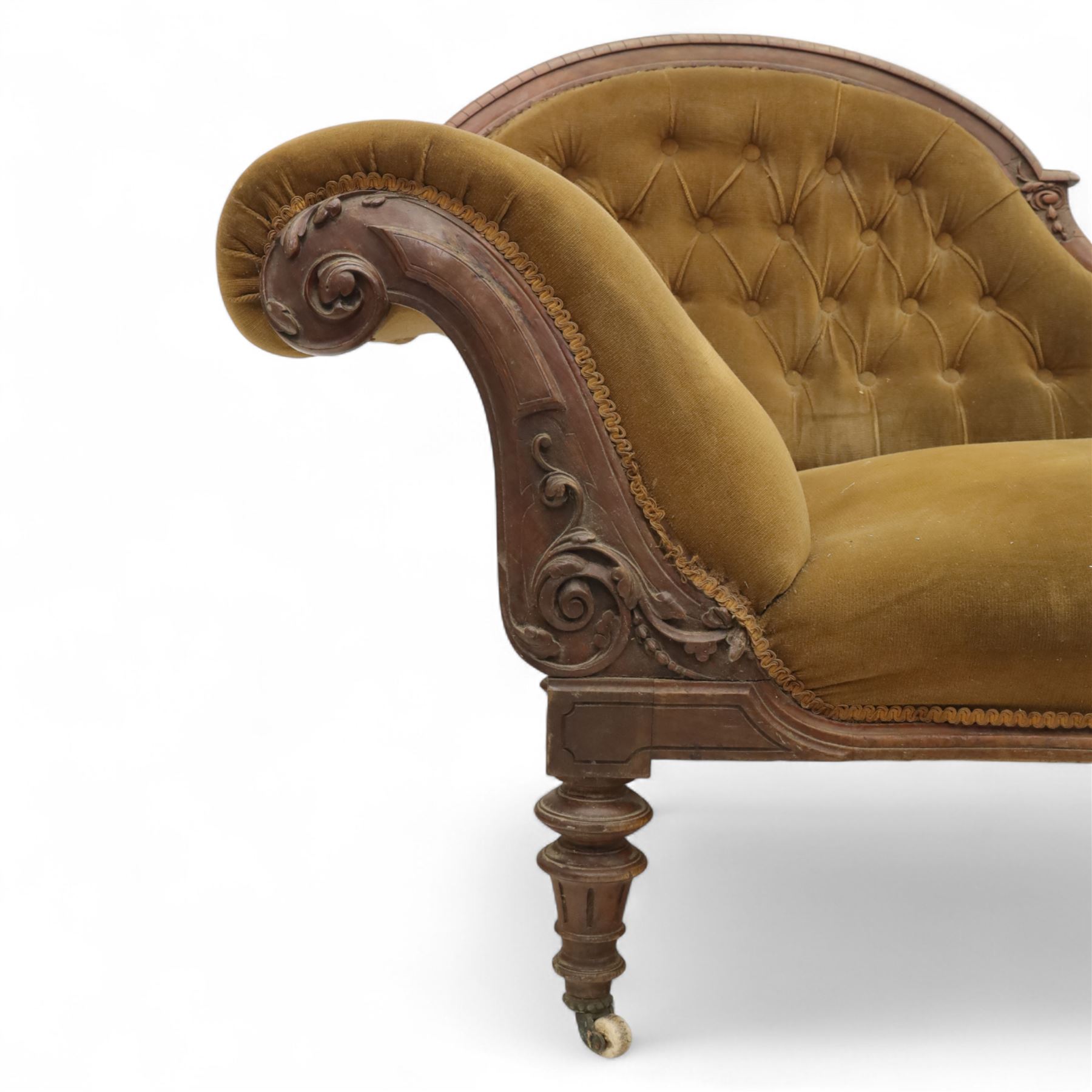 Victorian walnut framed Chaise longue, with carved scroll decoration and an out-swept buttoned upholstered, padded back and scroll end, seat upholstered mustard coloured velvet fabric, raised on turned legs with ceramic castors 
