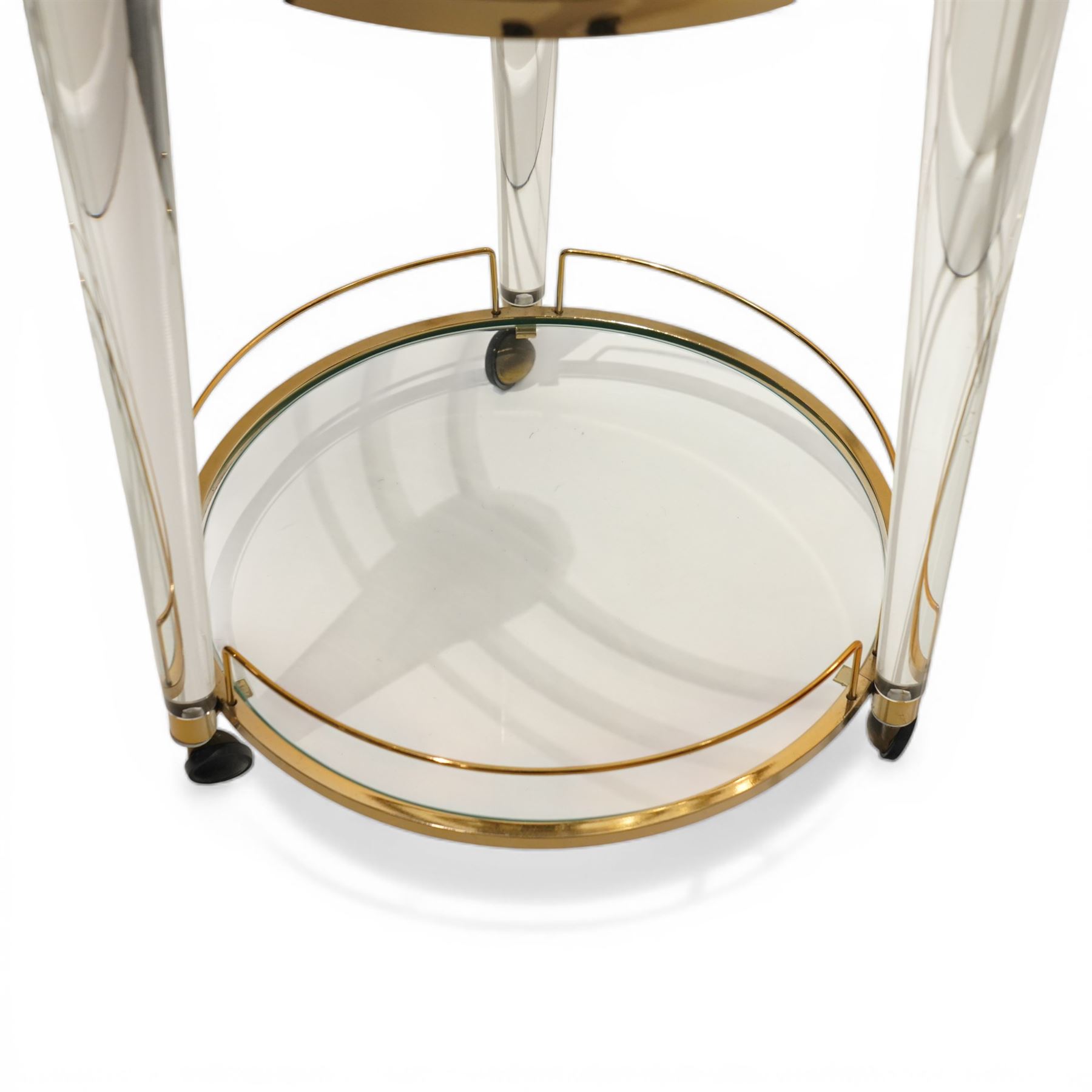 Hollywood Regency style gilt metal and glass serving trolley, circular top in a polished brass surround with three pineapple finials, supported on clear column legs, lower glass shelf enclosed by a brass gallery, terminating in castors