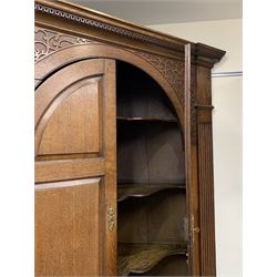 Large George III oak corner cupboard, projecting cornice over two stepped arch doors with fielded panels and blind fret work spandrels, flanked by fluted uprights, cupboard below enclosed by two fielded panel doors, the painted interior fitted with shaped shelves
 