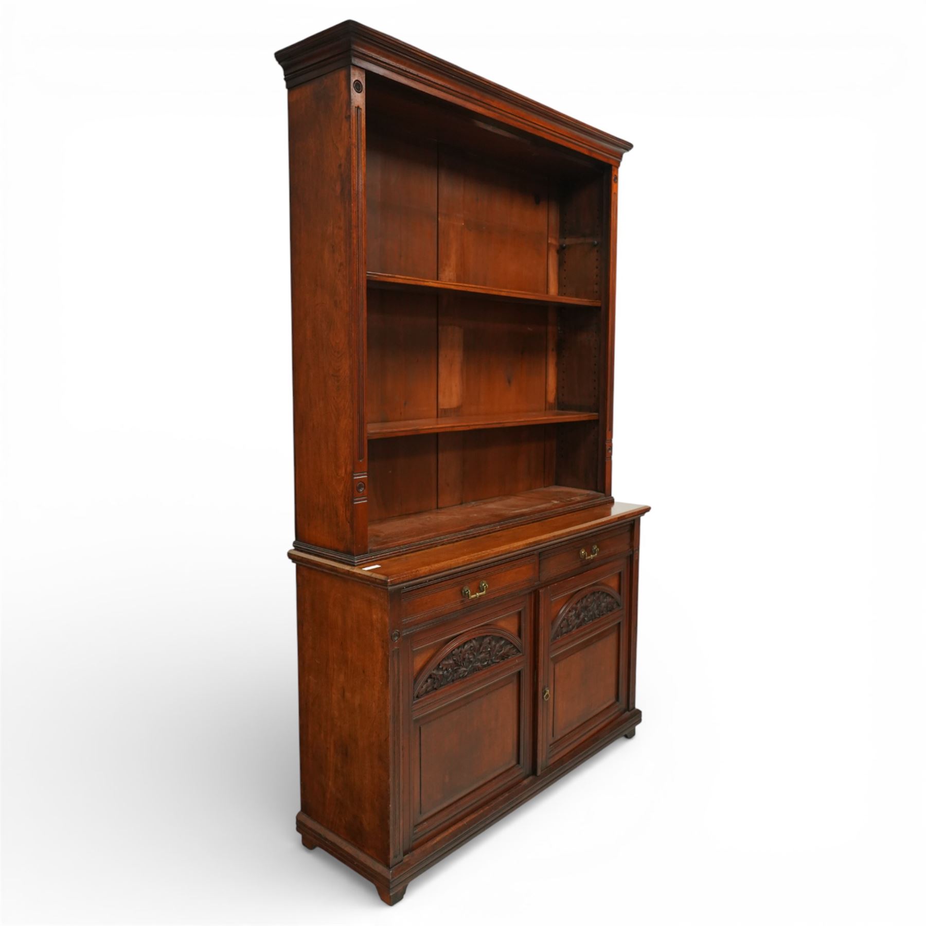 Late Victorian tall walnut open bookcase on cupboard, projecting cavetto cornice over reeded and fluted uprights moulded with roundel motifs, flanking two adjustable shelves, the base fitted with two drawers over panelled cupboards, carved with oakleaf and acorn motifs and grapevines, on bracket feet