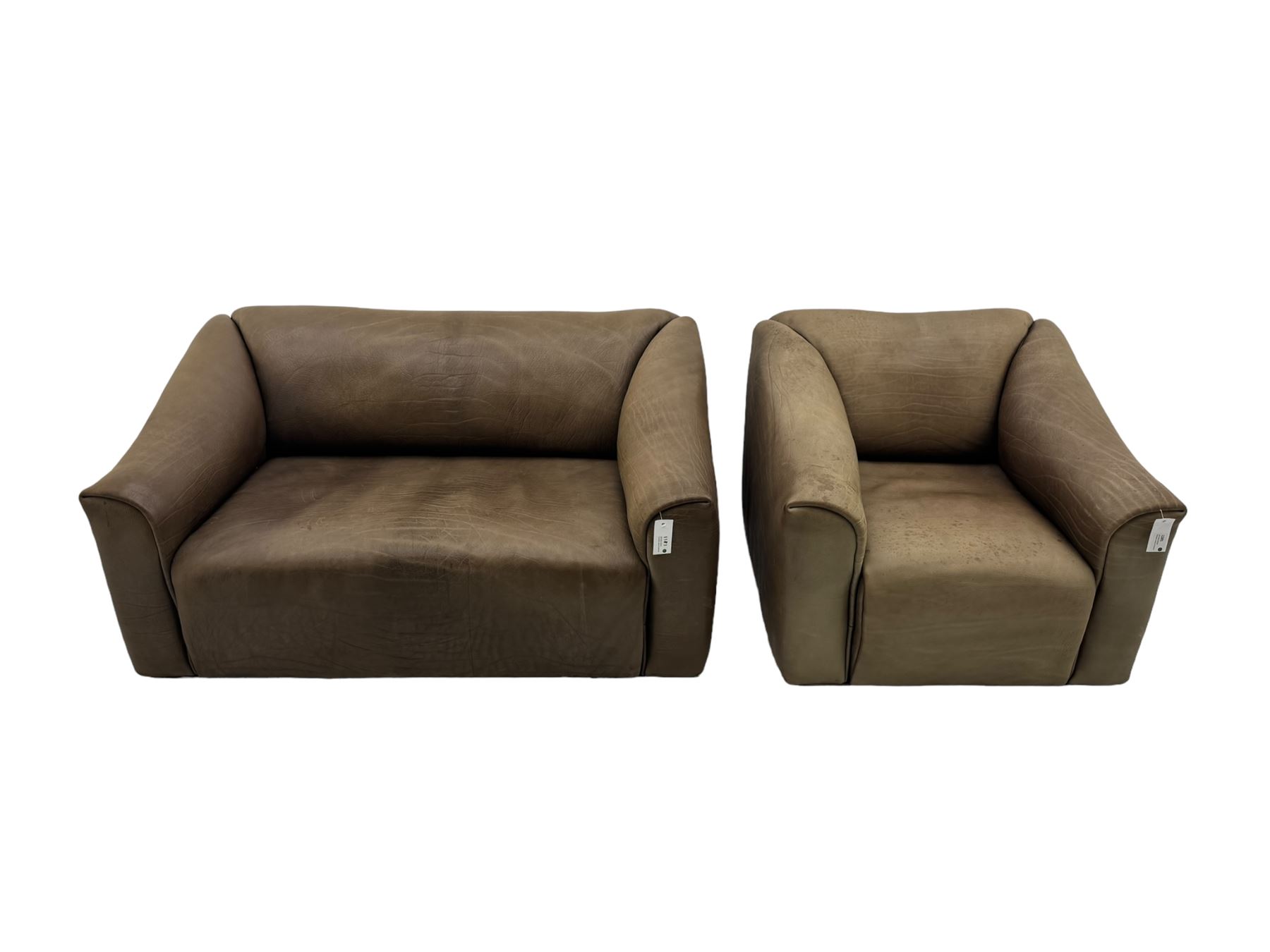 Mid-20th century two seater sofa, upholstered in soft brown leather with visible patina, curved arms and low back, on concealed supports (W138cm, D86cm, H72cm); matching armchair (W84cm, D86cm, H72cm)